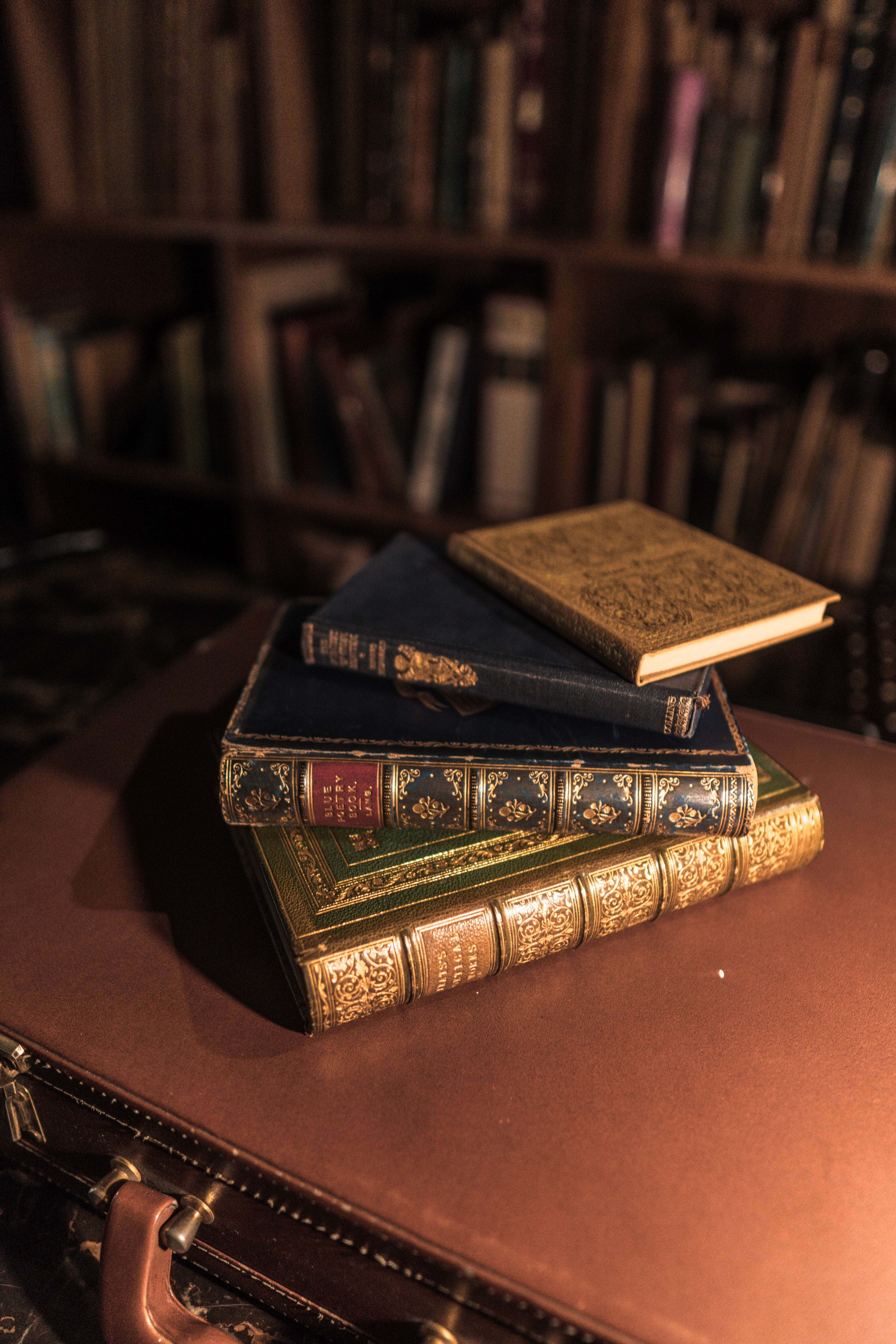 literature 桌布 壁紙 — 一堆華麗的復古書籍放在一個皮革行李箱上，位於一個光線昏暗、有木質書架的圖書館中。