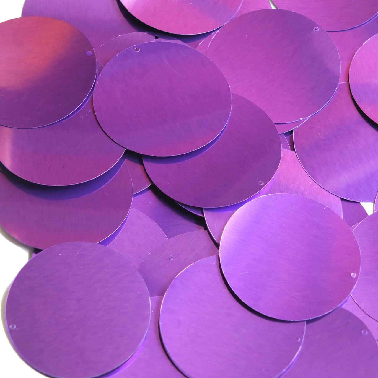Purple Sequins 桌布 壁紙 — 一堆閃亮金屬紫色圓形碟片散落在白色表面上，光線柔和。