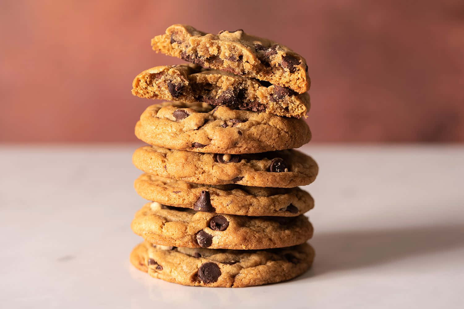 Cookie 桌布 壁紙 — 一堆高高的金黃色朱古力曲奇，其中一塊折成兩半，露出黏稠的融化朱古力。