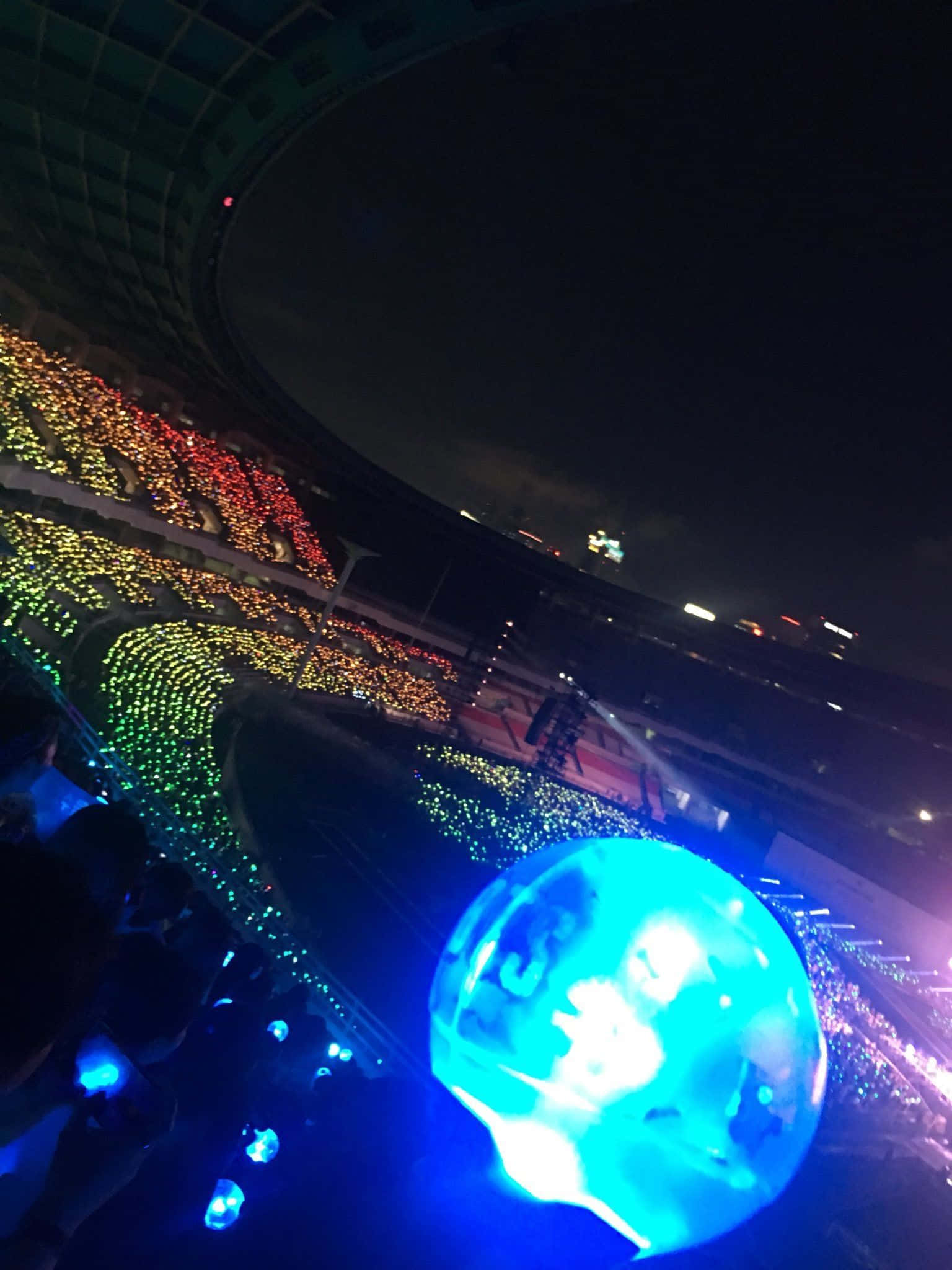 Bts Army Bomb 桌布 壁紙 — 一場令人眼花繚亂的夜間演唱會，粉絲們手持發光燈光，在巨大的體育場中形成色彩繽紛的圖案。