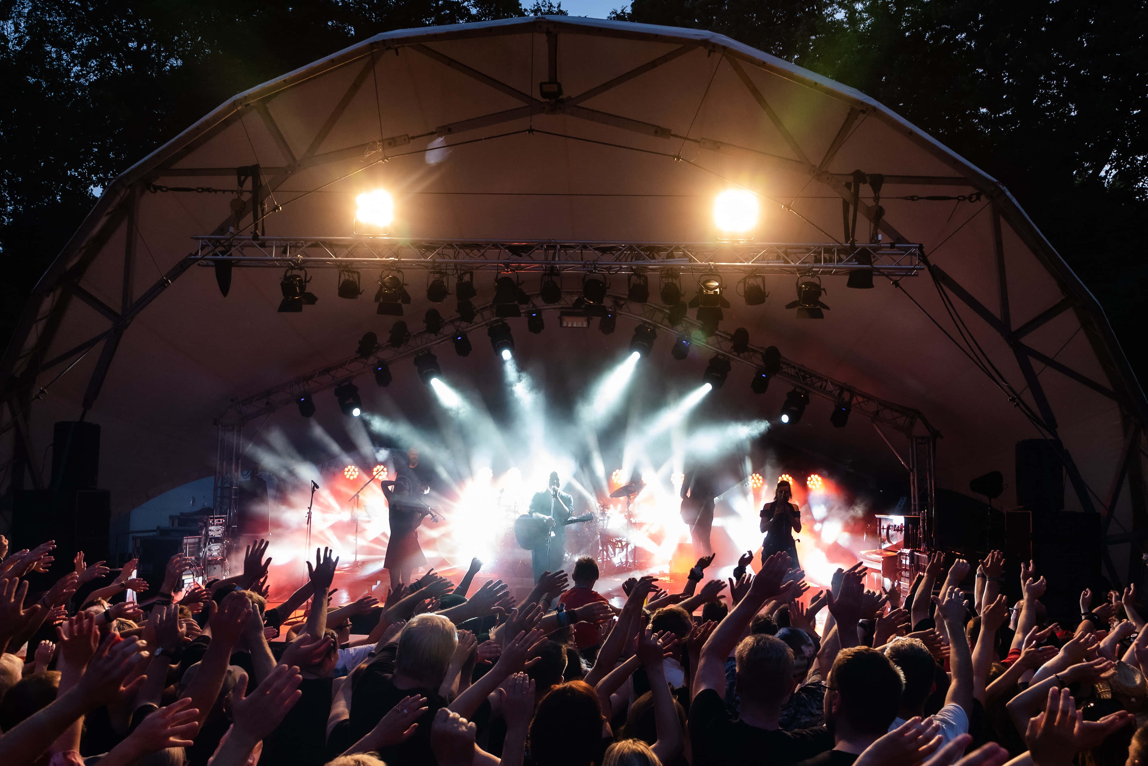 music festival 桌布 壁紙 — 一場充滿活力的戶外音樂會，在帳篷下進行，明亮的舞台燈光照亮表演者和熱情高舉雙手的觀眾。