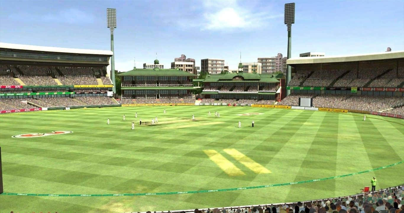Cricket 桌布 壁紙 — 一場充滿活力的板球比賽在精心條紋的綠色場地上展開，藍天白雲下，體育場人群歡呼。