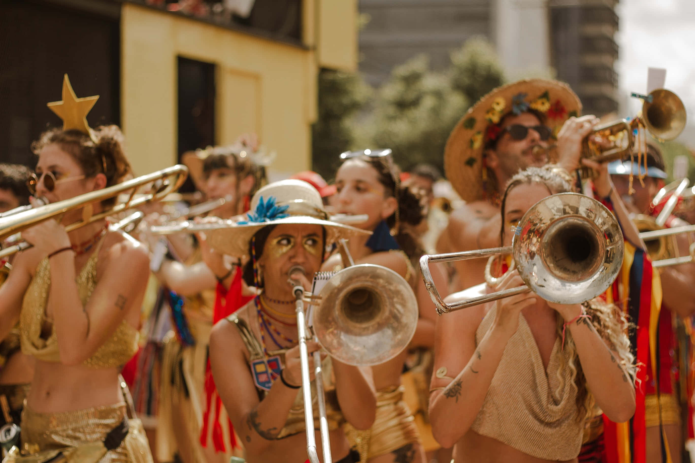 music festival 桌布 壁紙 — 一場充滿活力的街頭巡遊，身穿金色服裝的音樂家在明亮的日光下演奏長號和小號。
