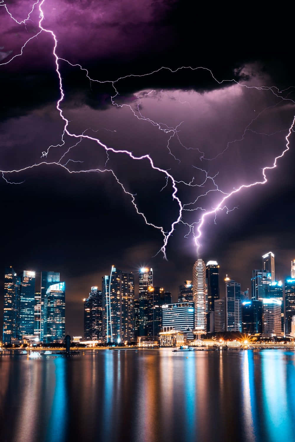 Thunderstorm 桌布 壁紙 — 一場戲劇性的夜間風暴，生動的紫色閃電照亮了現代城市天際線，倒映在平靜的水面上。