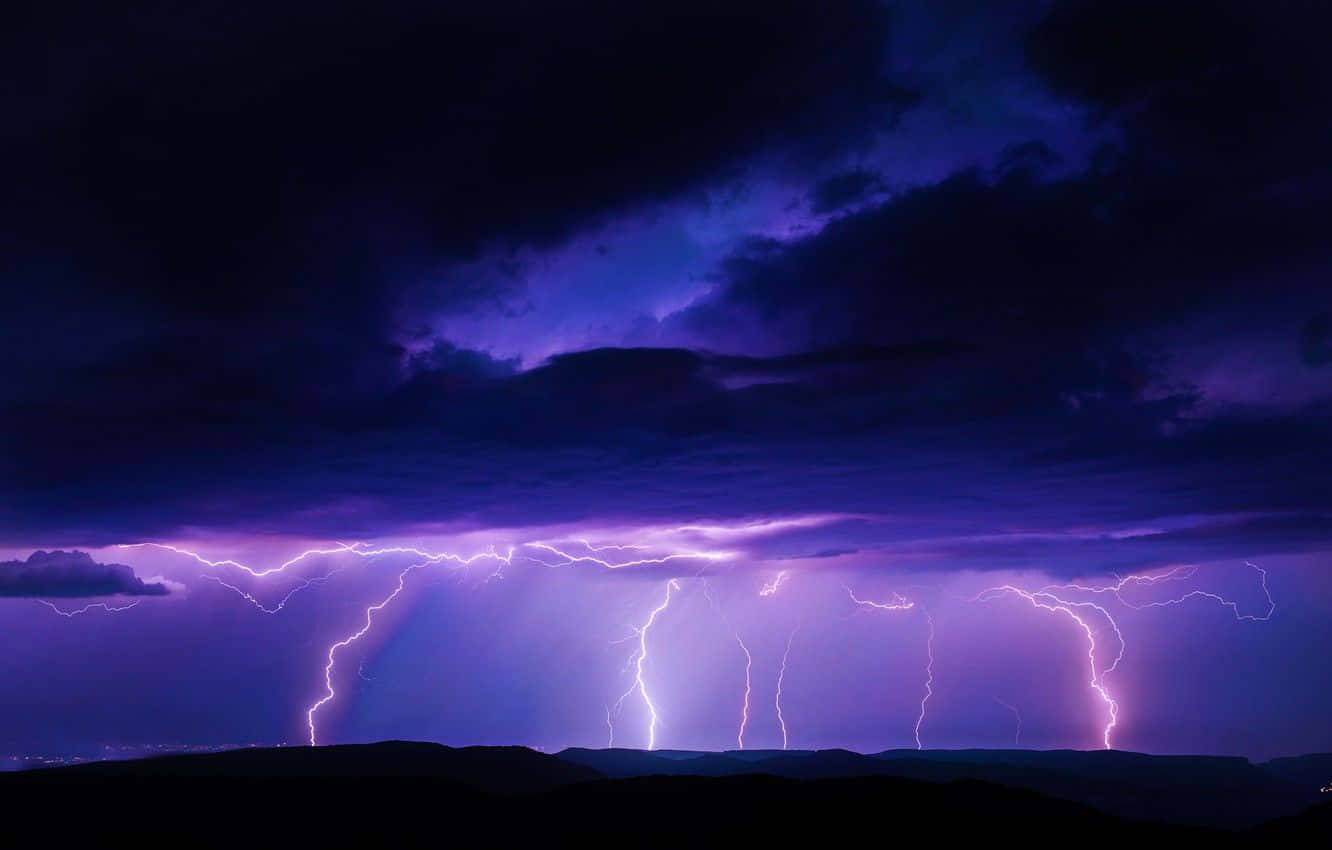Thunderstorm 桌布 壁紙 — 一場戲劇性的紫色閃電風暴照亮了夜晚黑暗天空中輪廓分明的山脈。