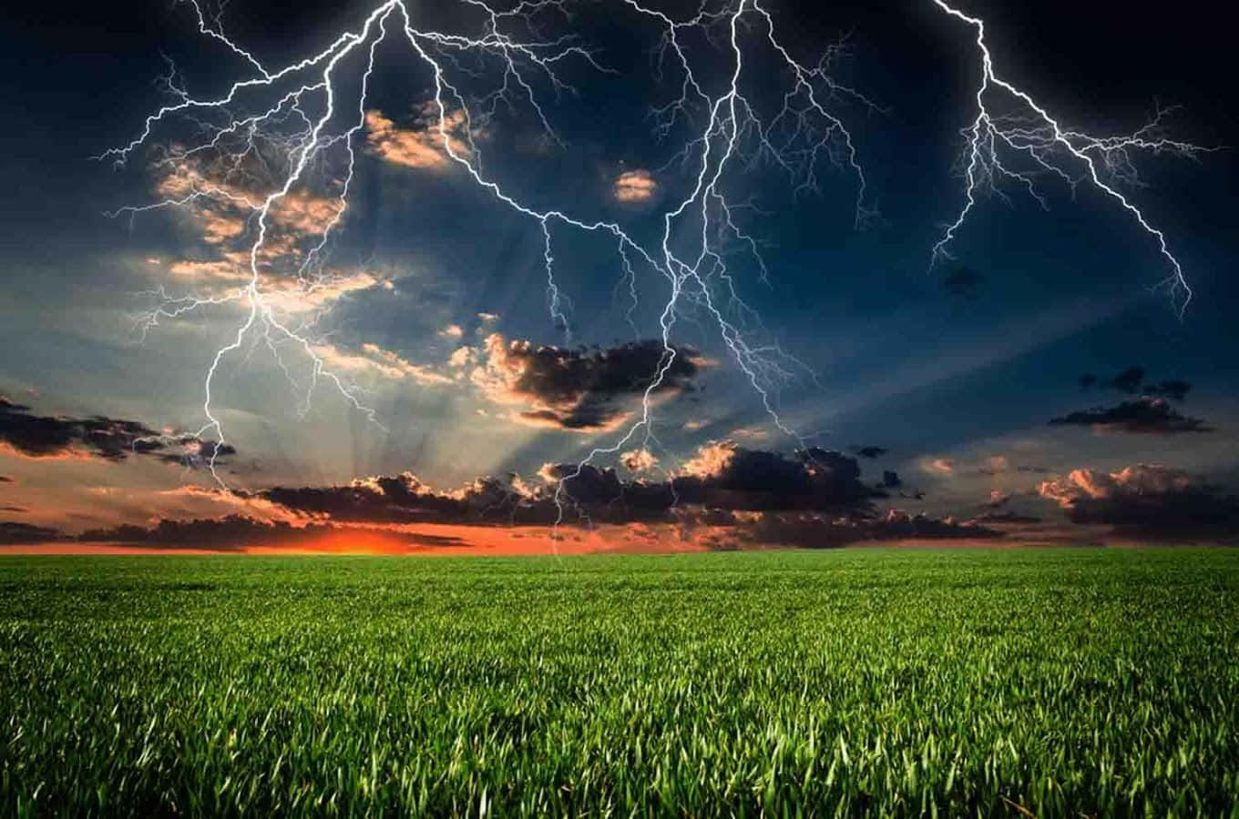 雷暴 桌布 壁紙 — 一場戲劇性的雷暴照亮了日落時分廣闊的綠色田野，耀眼的光芒穿透烏雲。