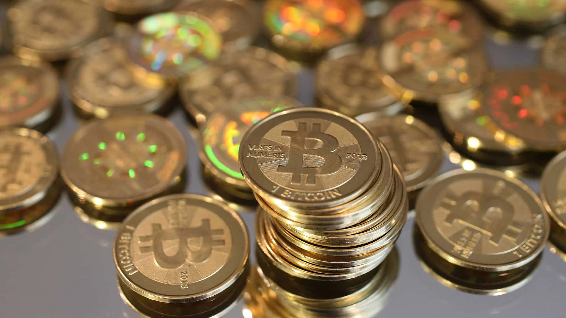 一場數位貨幣革命 壁紙 — 一堆閃亮金色比特幣硬幣帶有全息彩虹圖案，放置在反光表面上。