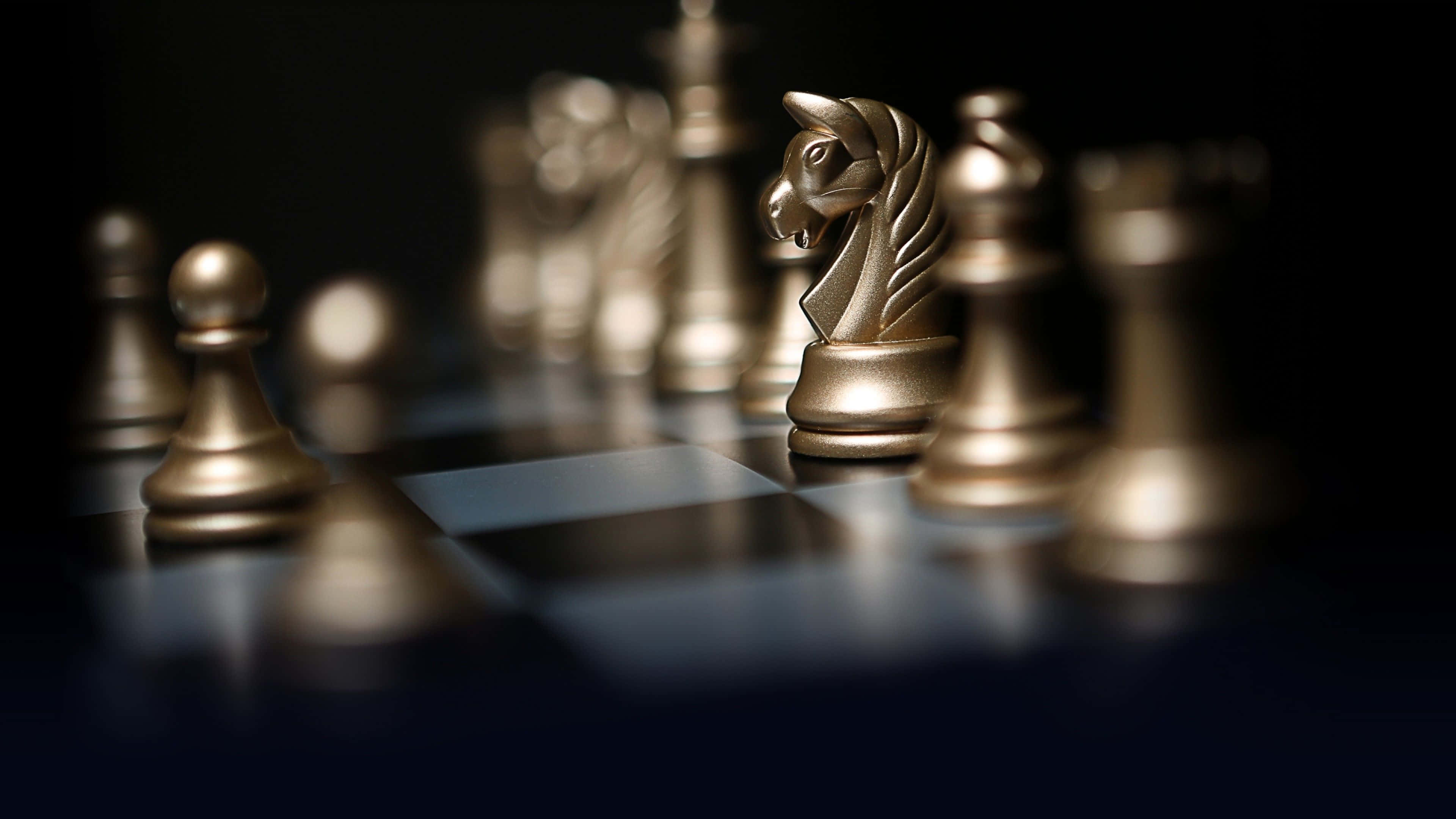一場激烈的象棋對決 壁紙 — 金色國際象棋棋子在戲劇性燈光下於深色棋盤上閃耀，淺景深突顯前景的騎士。