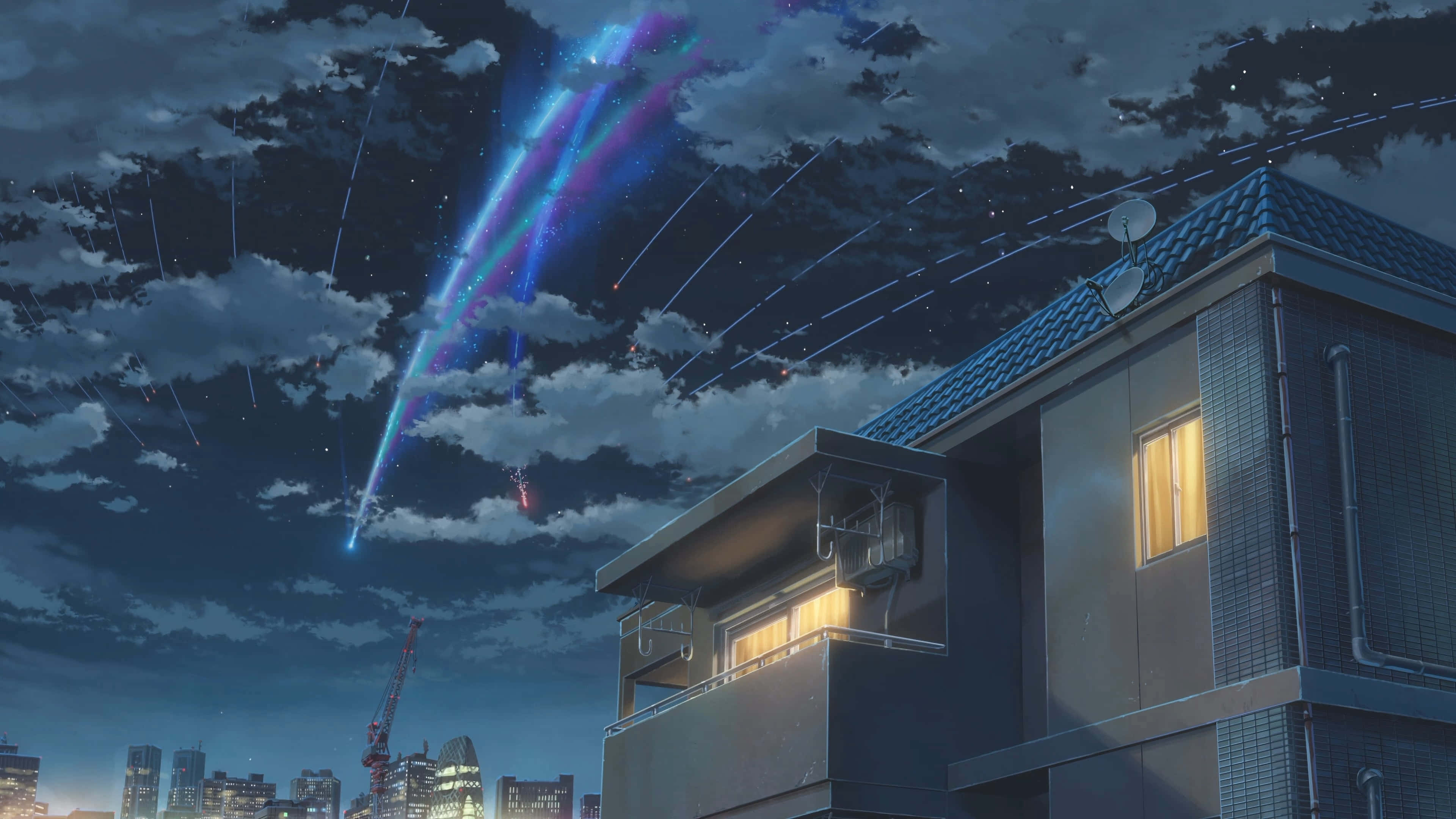 Makoto Shinkai 桌布 壁紙 — 一場發光的宇宙流星雨劃過多雲的夜空，下方是寧靜的住宅樓宇，窗戶透出溫暖的燈光。