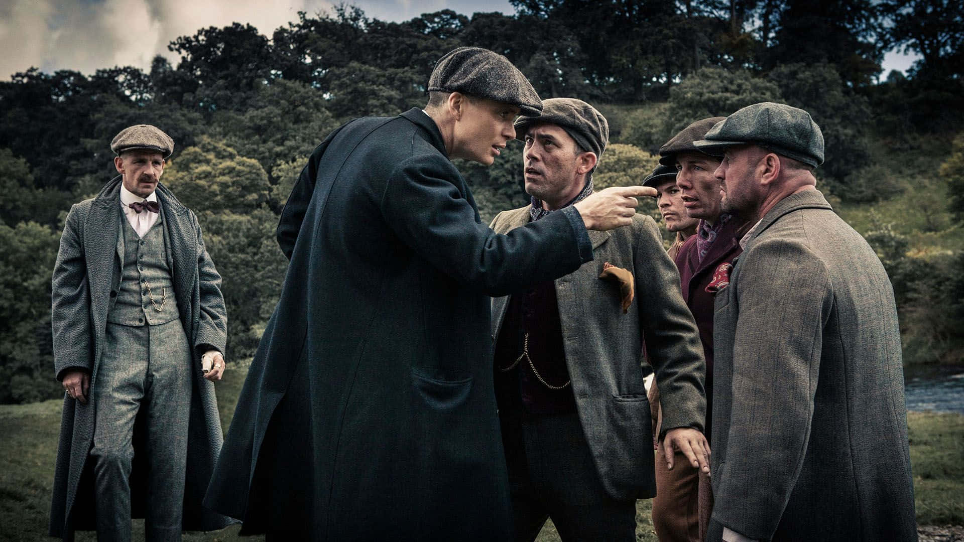 Peaky Blinders 桌布 壁紙 — 一場緊張的對峙展開，一名身穿深色大衣的男子在五名穿著復古粗花呢西裝和扁平帽的男子組成的群體中，指責性地指向另一名男子。