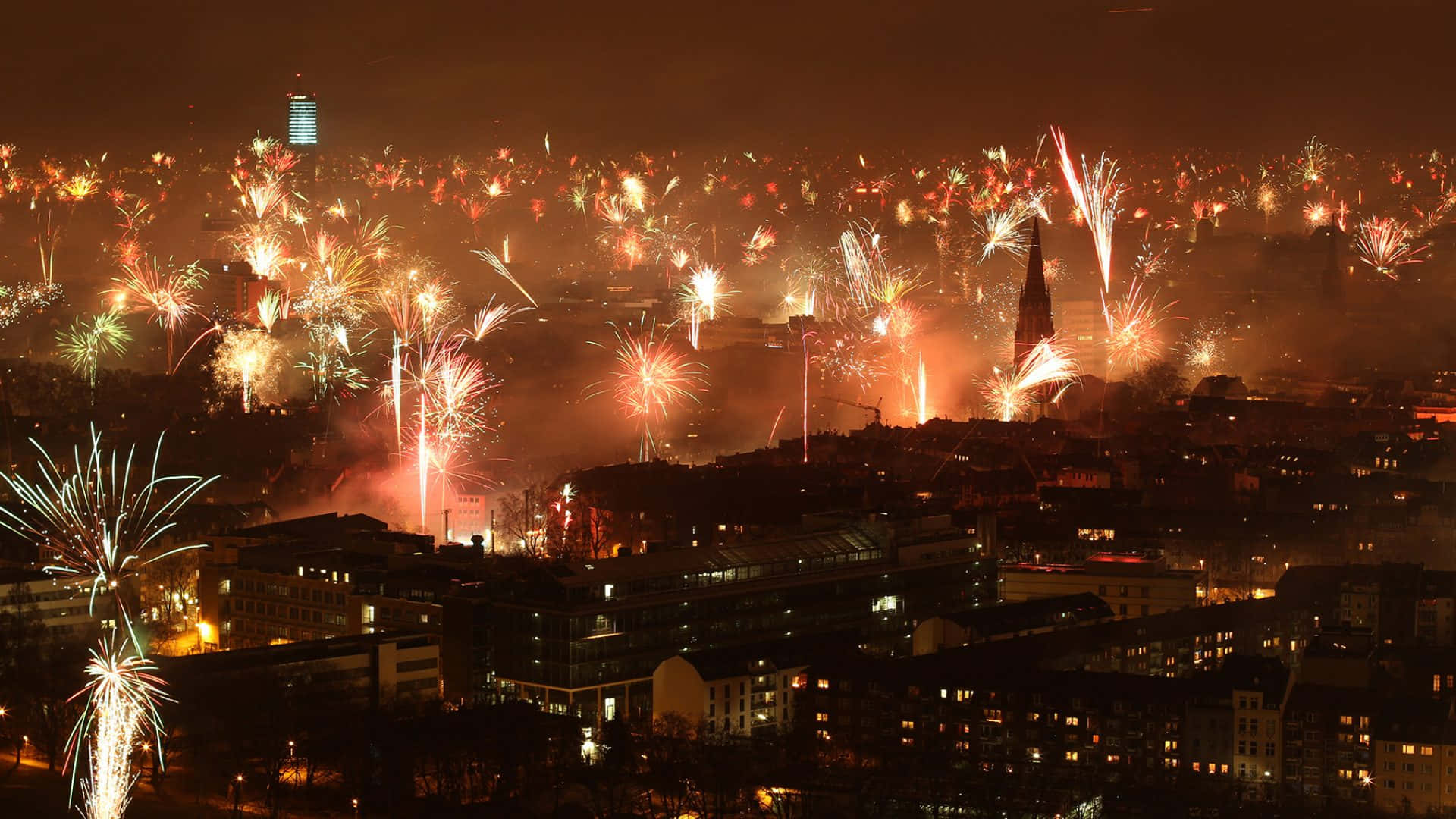 煙花在夜間城市上空綻放，下方建築物燈火通明。 — 新年動畫 壁紙