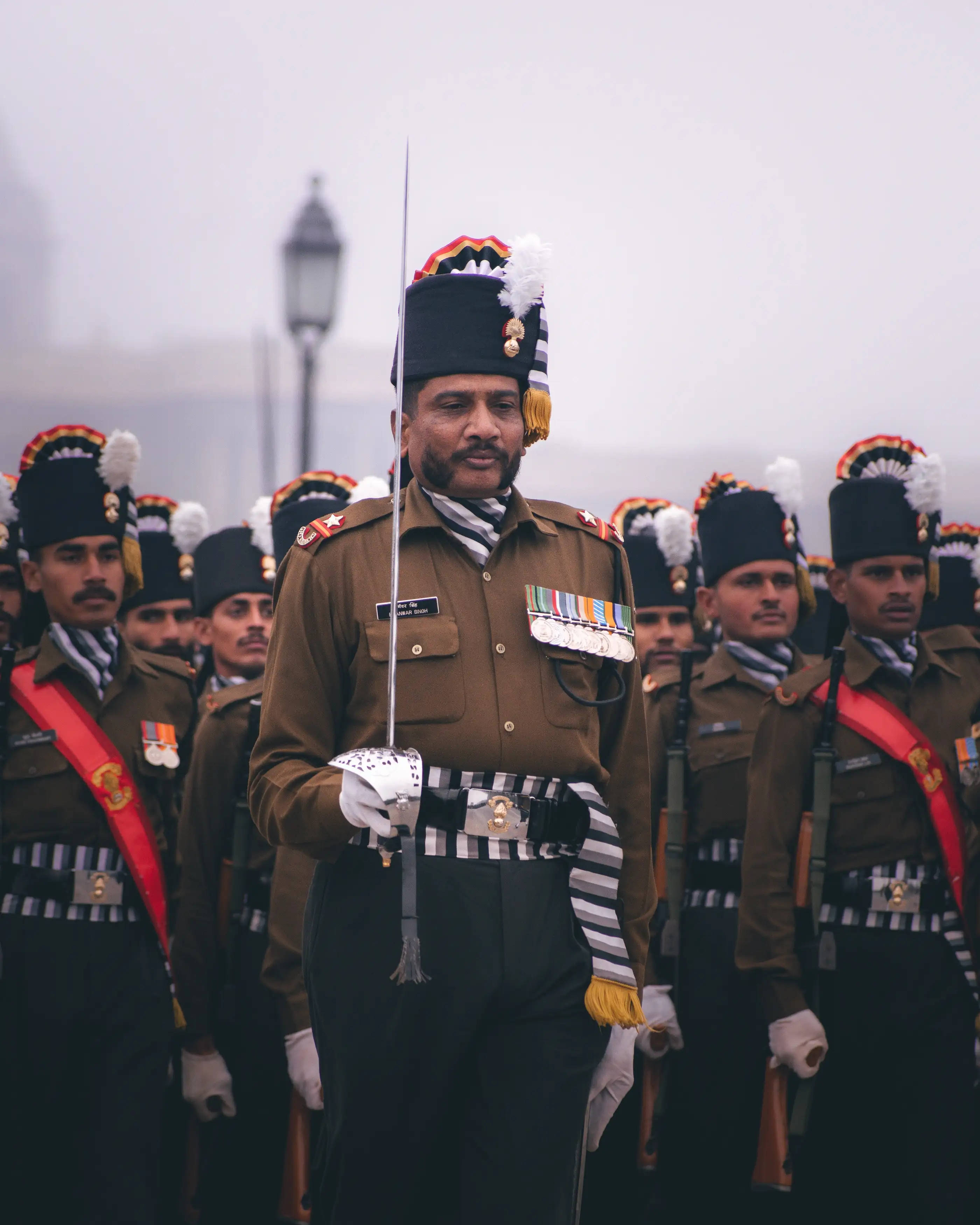 Indian Army 桌布 壁紙 — 一場莊嚴的軍事閱兵，身穿禮儀制服的士兵在朦朧的天空下持步槍。