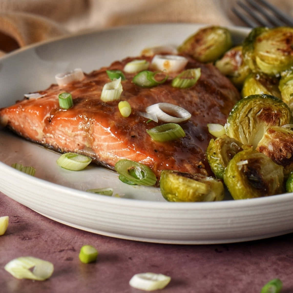 Salmon 桌布 壁紙 — 一塊光澤的釉面三文魚柳，上面放有切片青蔥，旁邊是烤抱子甘藍，放在白色碟子上。