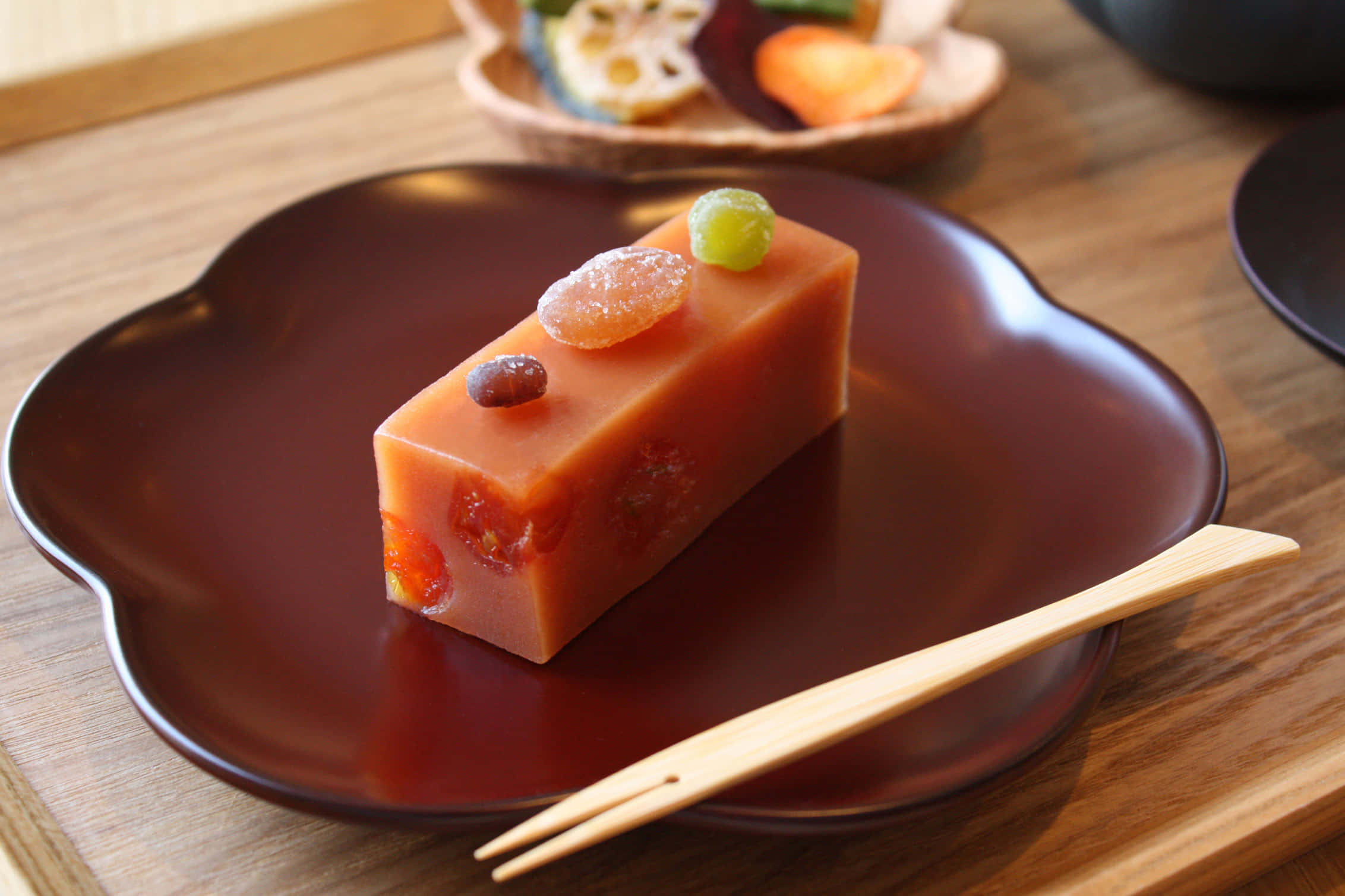 Japanese Sweets 桌布 壁紙 — 一塊半透明橙色日式麻糬甜點的長方形切片，上面放有蜜餞水果，置於深棕色花形碟上，旁邊有木筷子。