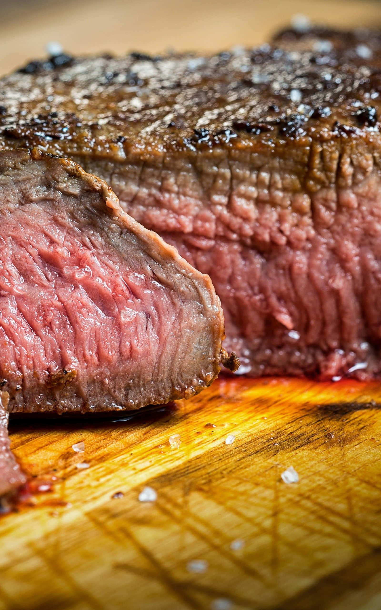 meat 桌布 壁紙 — 一塊多汁的 medium-rare 牛扒，帶有焦脆外皮，放在灑滿粗鹽的木砧板上。