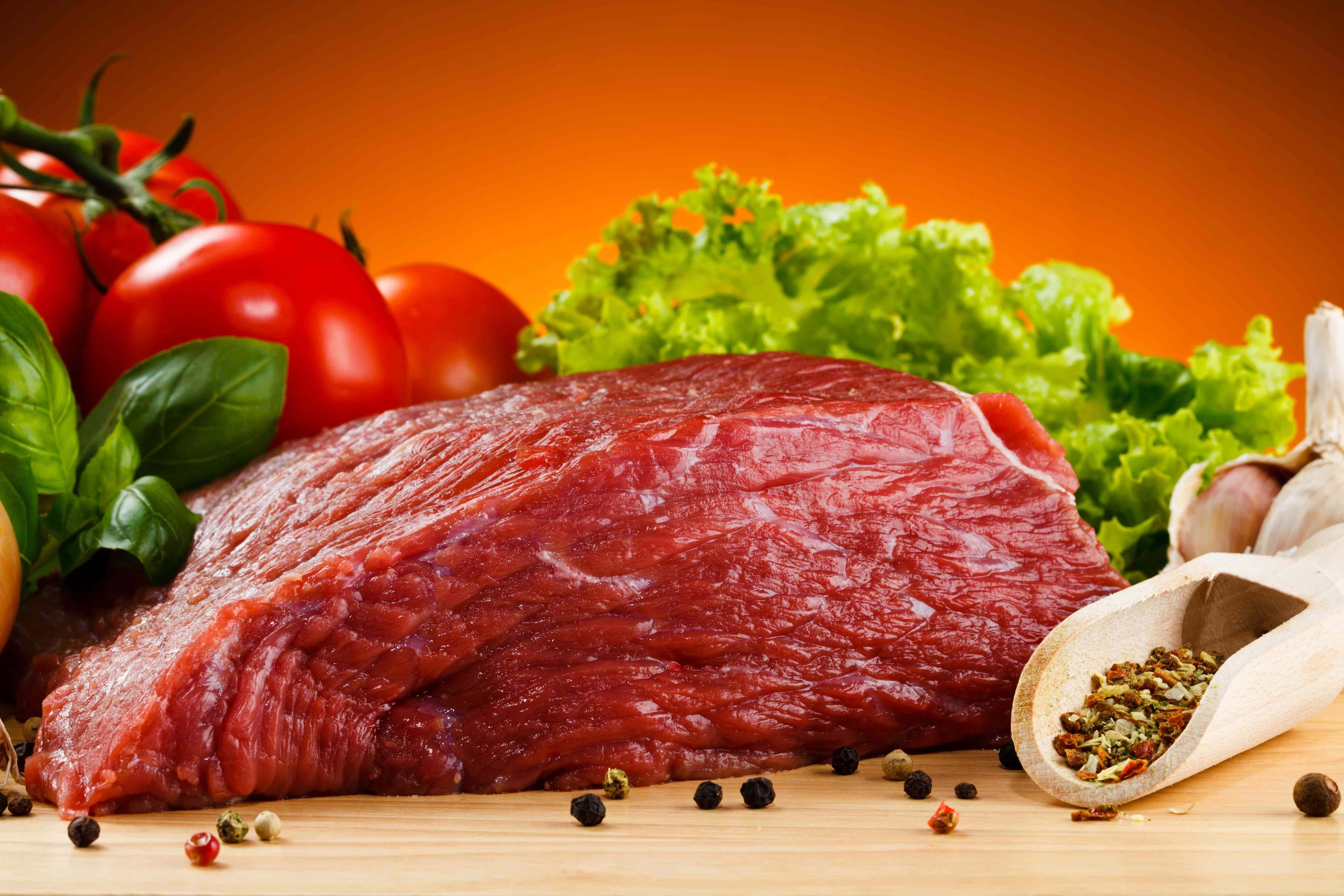 meat 桌布 壁紙 — 一塊多汁的生牛肉扒放在木板上，周圍是新鮮的番茄、羅勒、生菜、大蒜和胡椒粒，背景是溫暖的橙色。