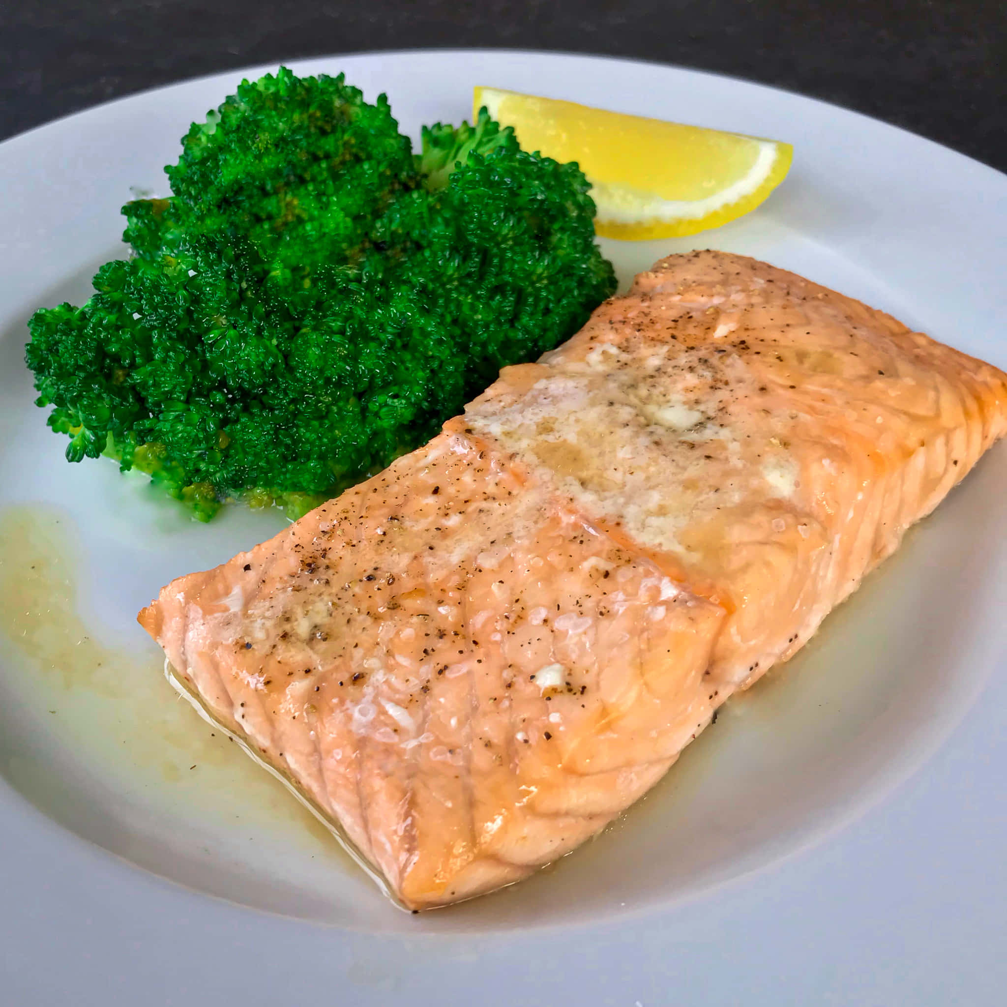 Salmon 桌布 壁紙 — 一塊完美烹調的三文魚柳，配上牛油和胡椒，旁邊放著鮮綠的西蘭花和檸檬角，置於白色碟上。