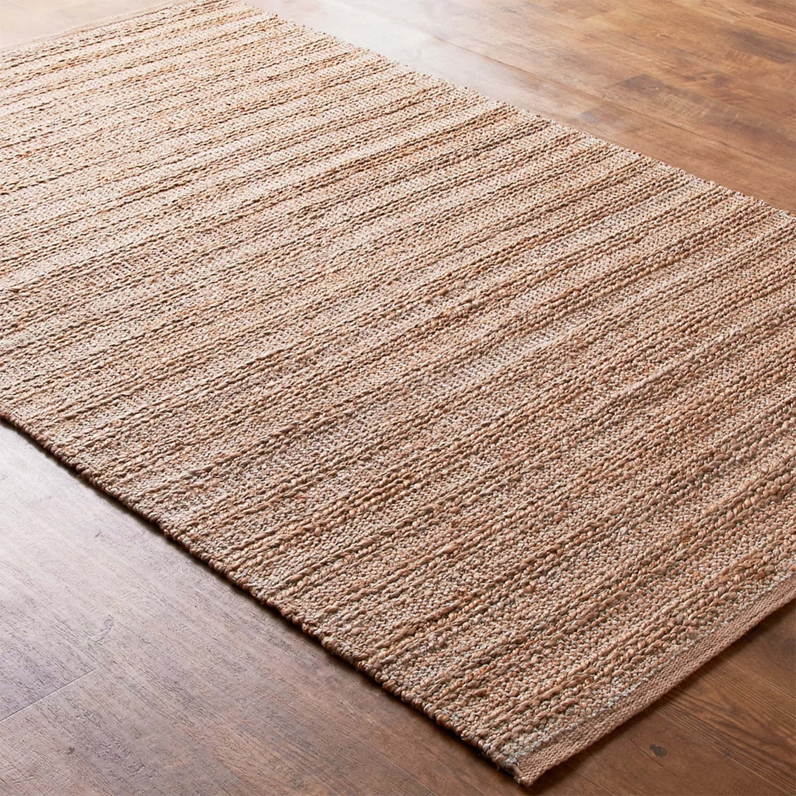 Carpet Texture 桌布 壁紙 — 一塊帶有天然纖維的質感米色編織地毯，斜放在暖色調的木地板上。