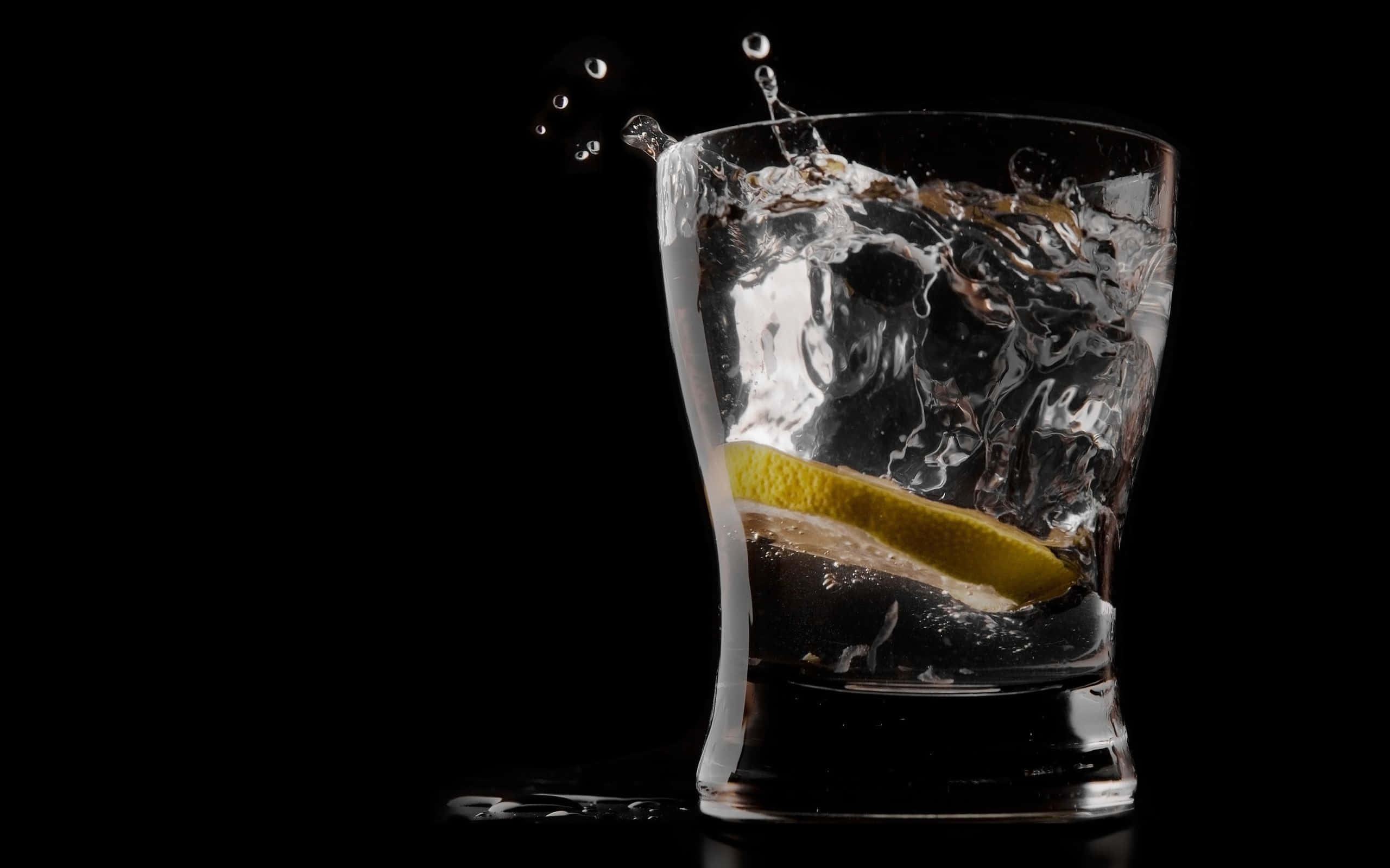 alcohol 桌布 壁紙 — 一塊檸檬楔形片濺入一杯清澈液體中，背景為純黑色。