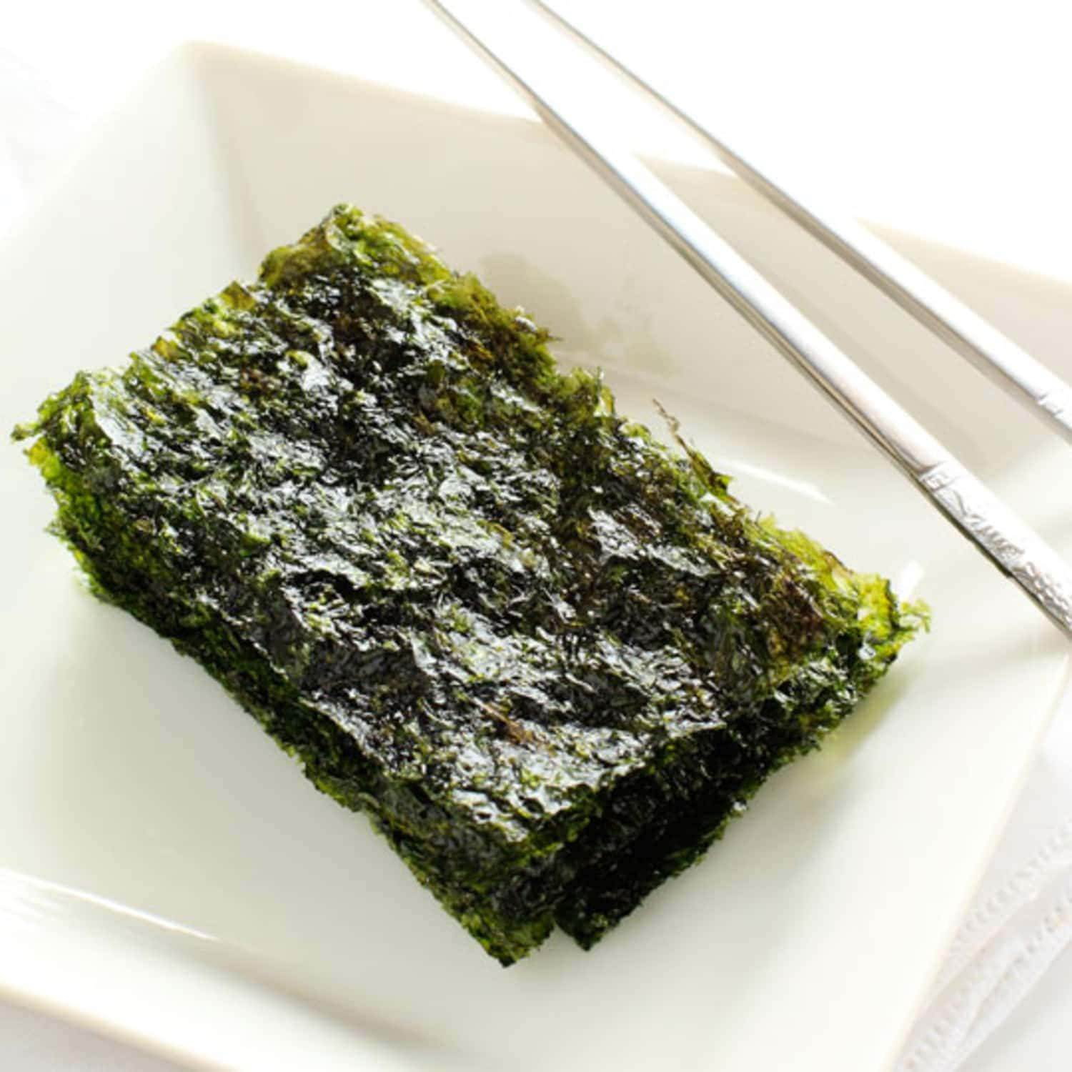 Seaweed 桌布 壁紙 — 一塊深綠色烤紫菜放在白色碟上，旁邊放著銀色筷子。