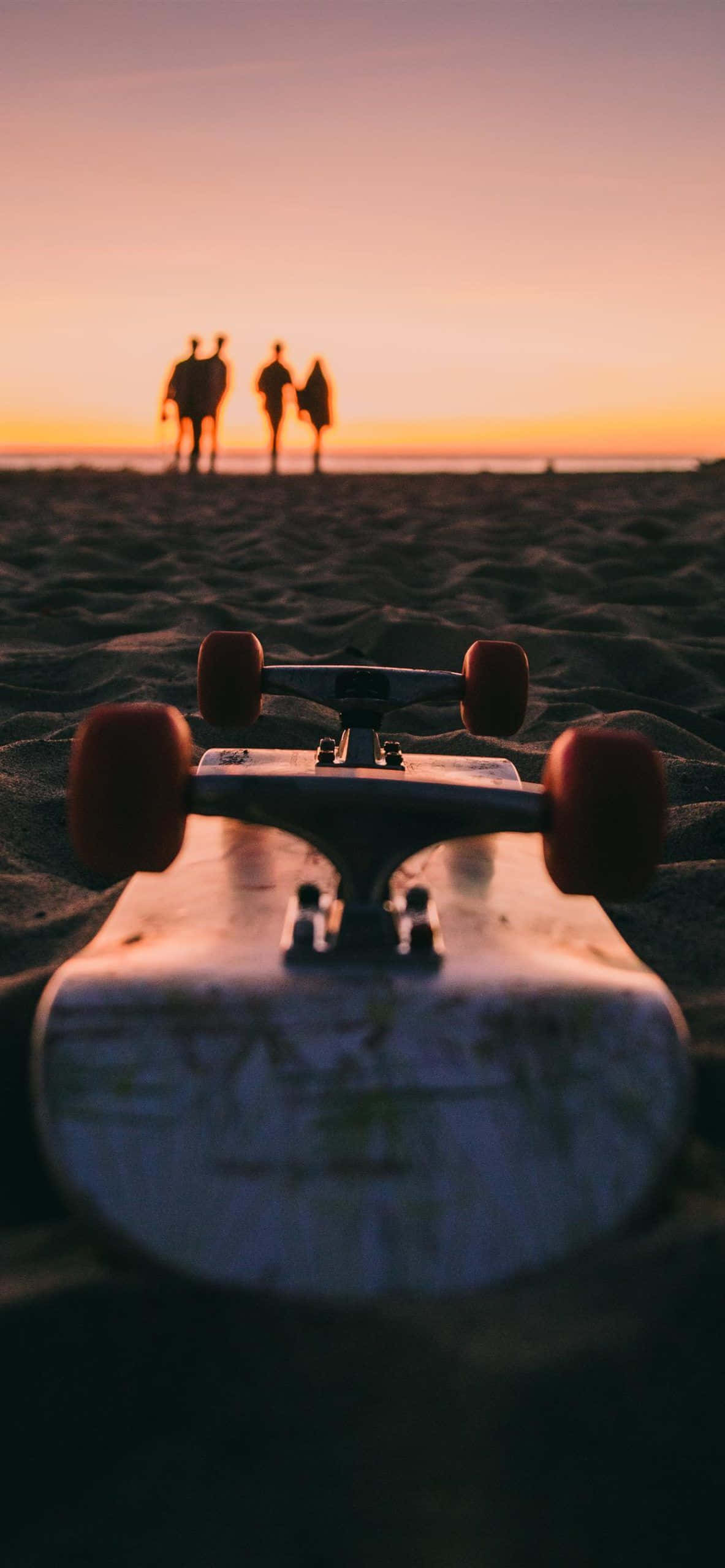 skateboarding 桌布 壁紙 — 一塊滑板擱在沙灘前景，三個剪影人物走向日落地平線。
