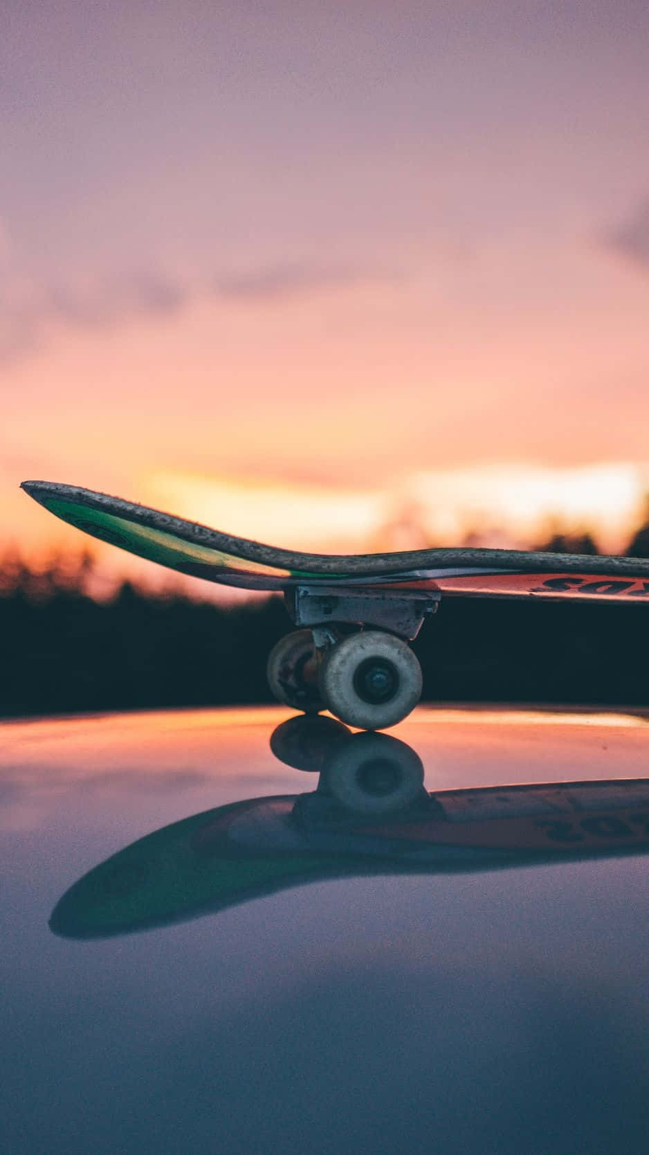 skateboarding 桌布 壁紙 — 一塊滑板放在光滑的表面上，反射出帶有柔和粉紅色和橙色色調的鮮豔日落天空。