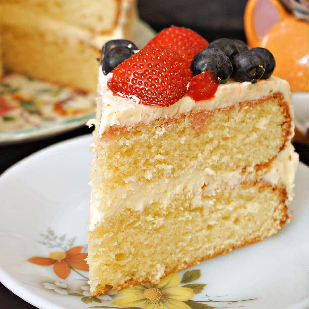 Buttercream 桌布 壁紙 — 一塊濕潤的層狀雲呢拿蛋糕片，上面放上新鮮草莓和藍莓，置於花卉圖案碟上。
