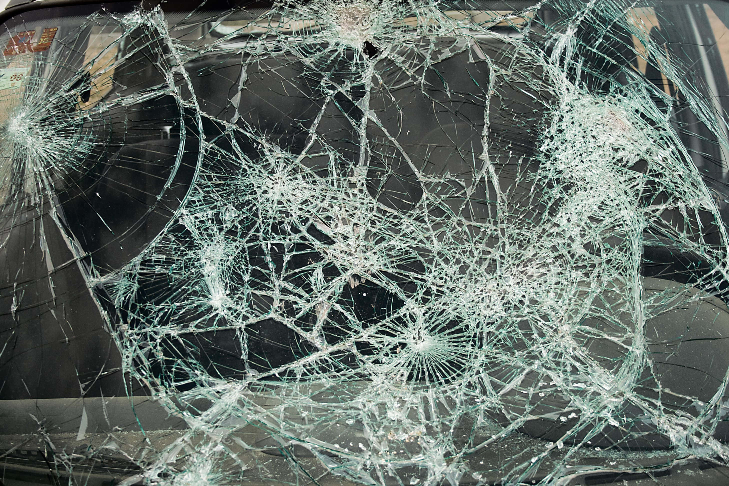 cracked 桌布 壁紙 — 一塊破碎的汽車擋風玻璃，帶有複雜的蜘蛛網狀裂紋，反射著柔和的白日光線。