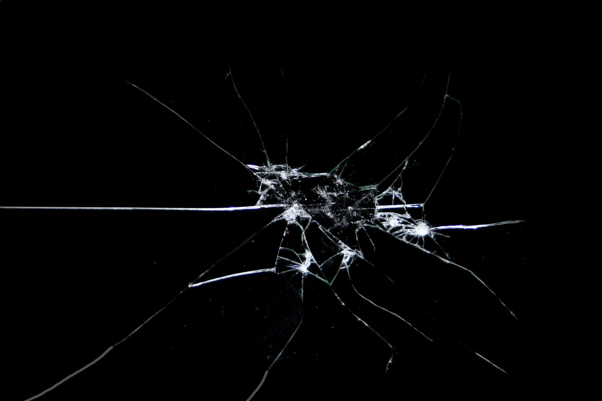 Broken Glass 桌布 壁紙 — 一塊破碎的玻璃表面，從中央撞擊點放射出複雜的裂紋，背景為純黑色。