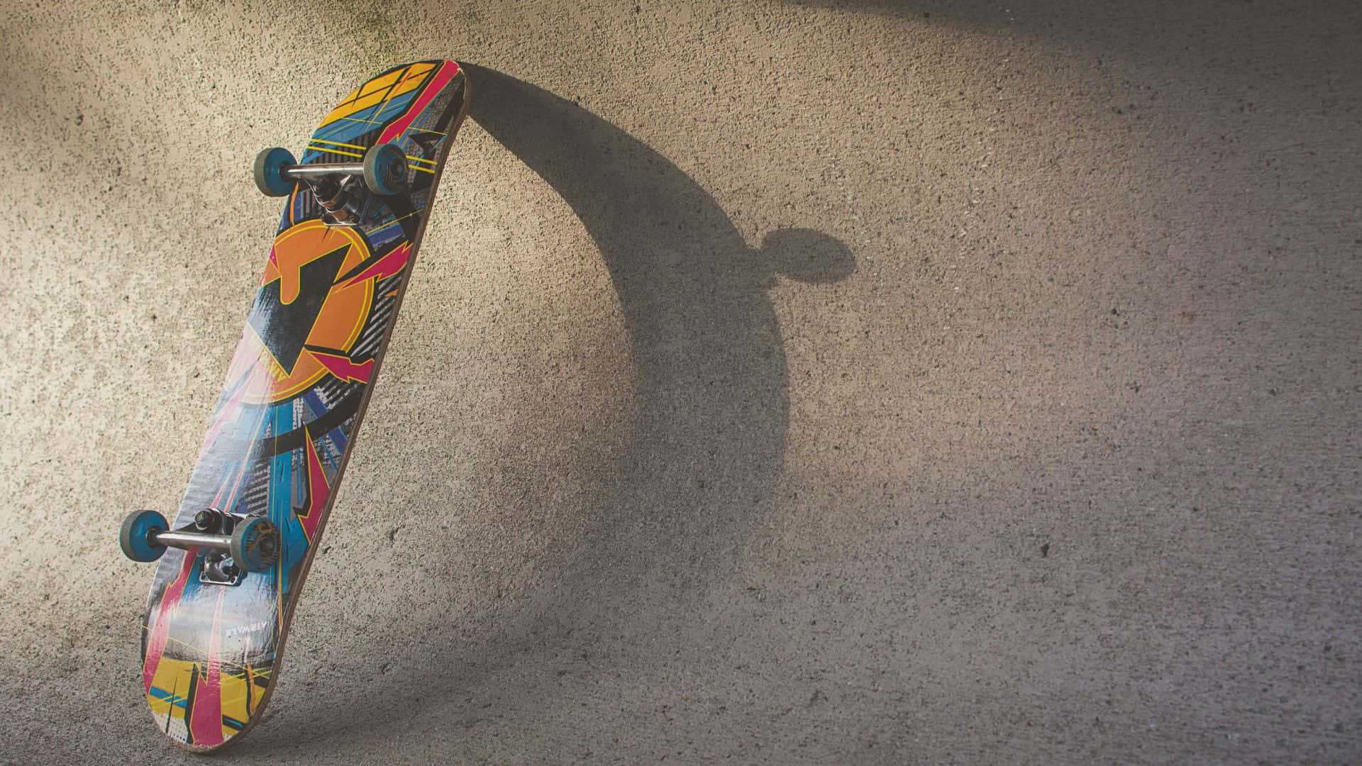 滑板 桌布 壁紙 — 一塊色彩鮮明的圖案滑板靠在混凝土上，在柔和日光下投下長長的影子。