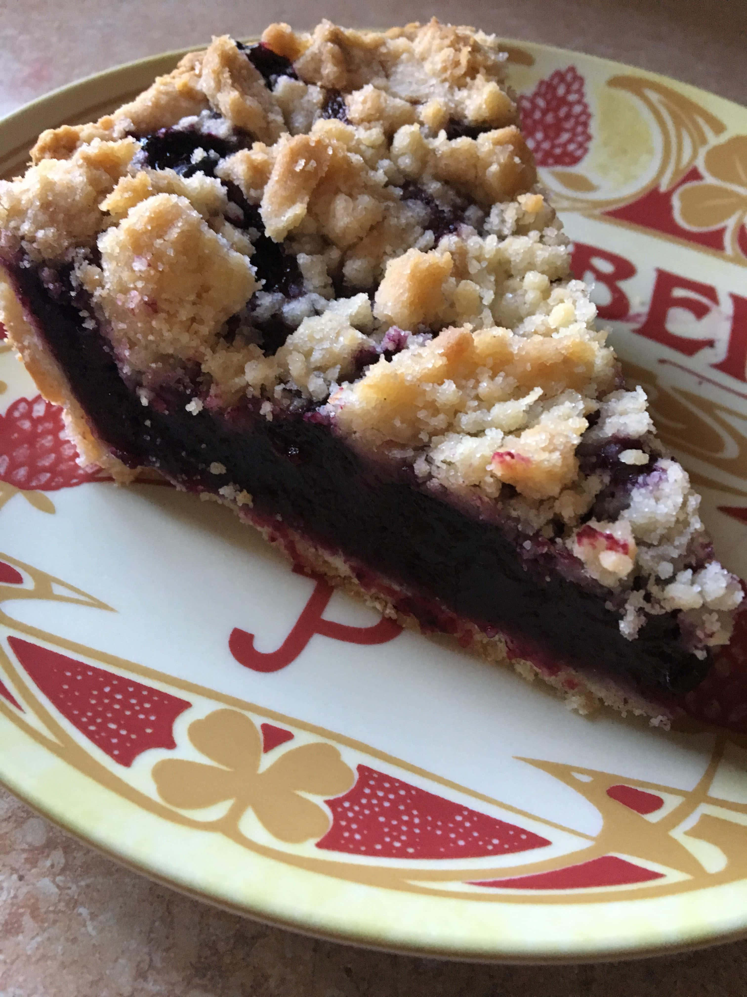 Blueberry Pie 桌布 壁紙 — 一塊藍莓金寶批的微距特寫，金黃酥皮放在有圖案的碟上。