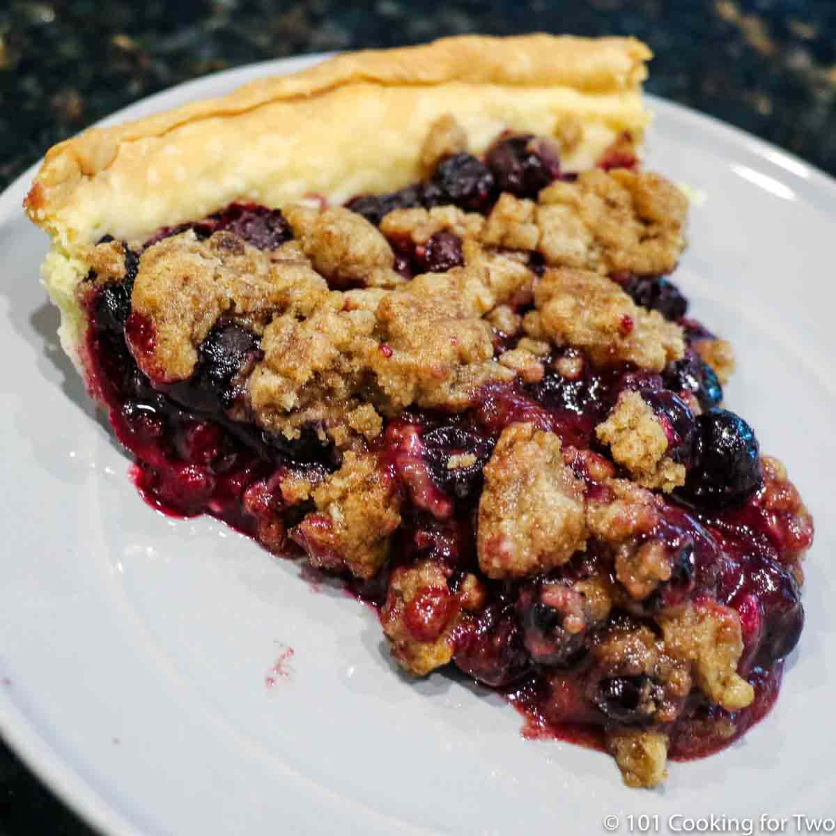 Blueberry Pie 桌布 壁紙 — 一塊藍莓金寶批的近鏡，金黃酥皮配上多汁莓果餡料，放在白色碟上。