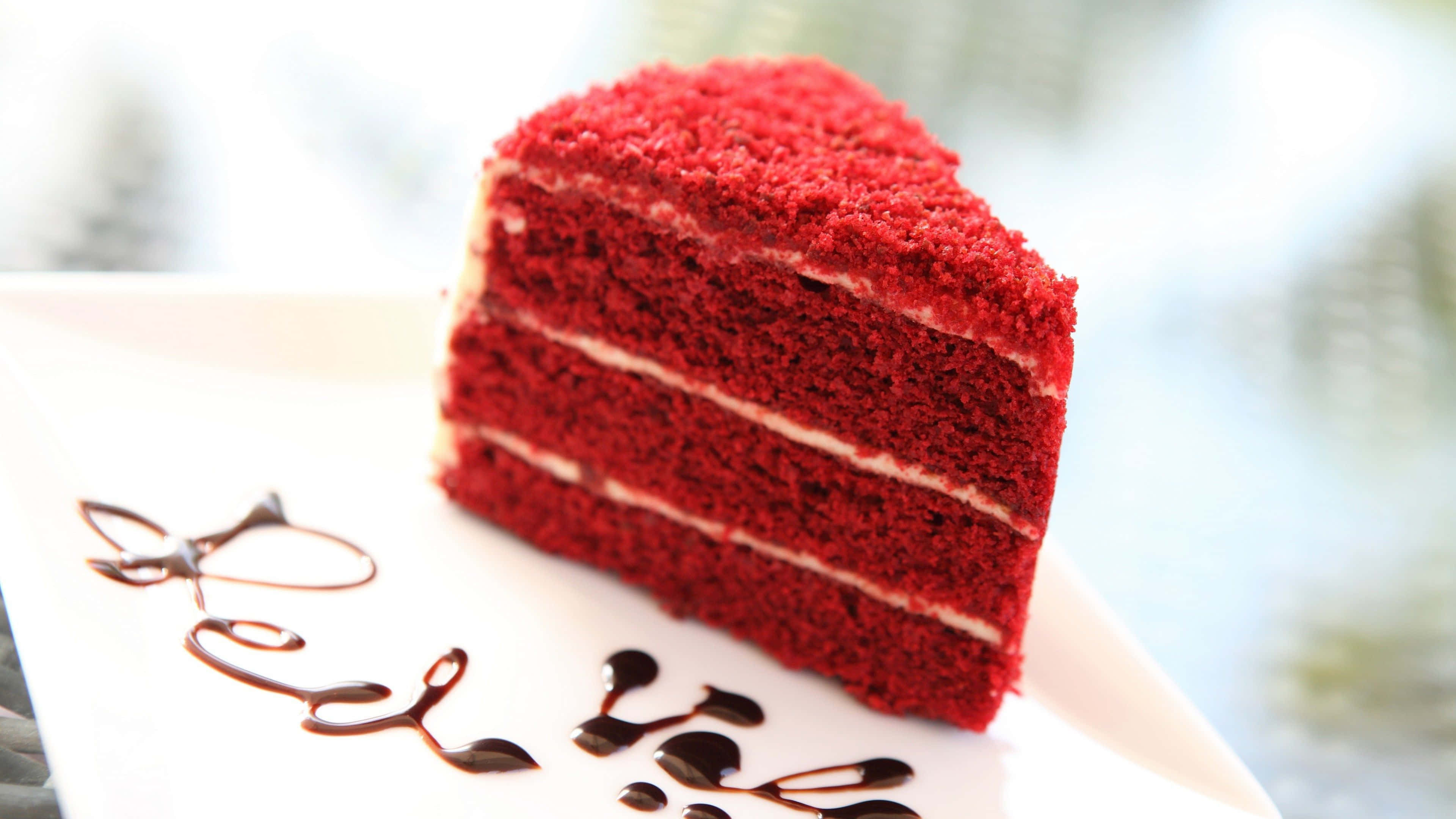 Red Velvet Cake 桌布 壁紙 — 一塊豐富的紅絲絨蛋糕切片，配以奶油芝士糖霜和朱古力淋醬，放在白色碟子上。