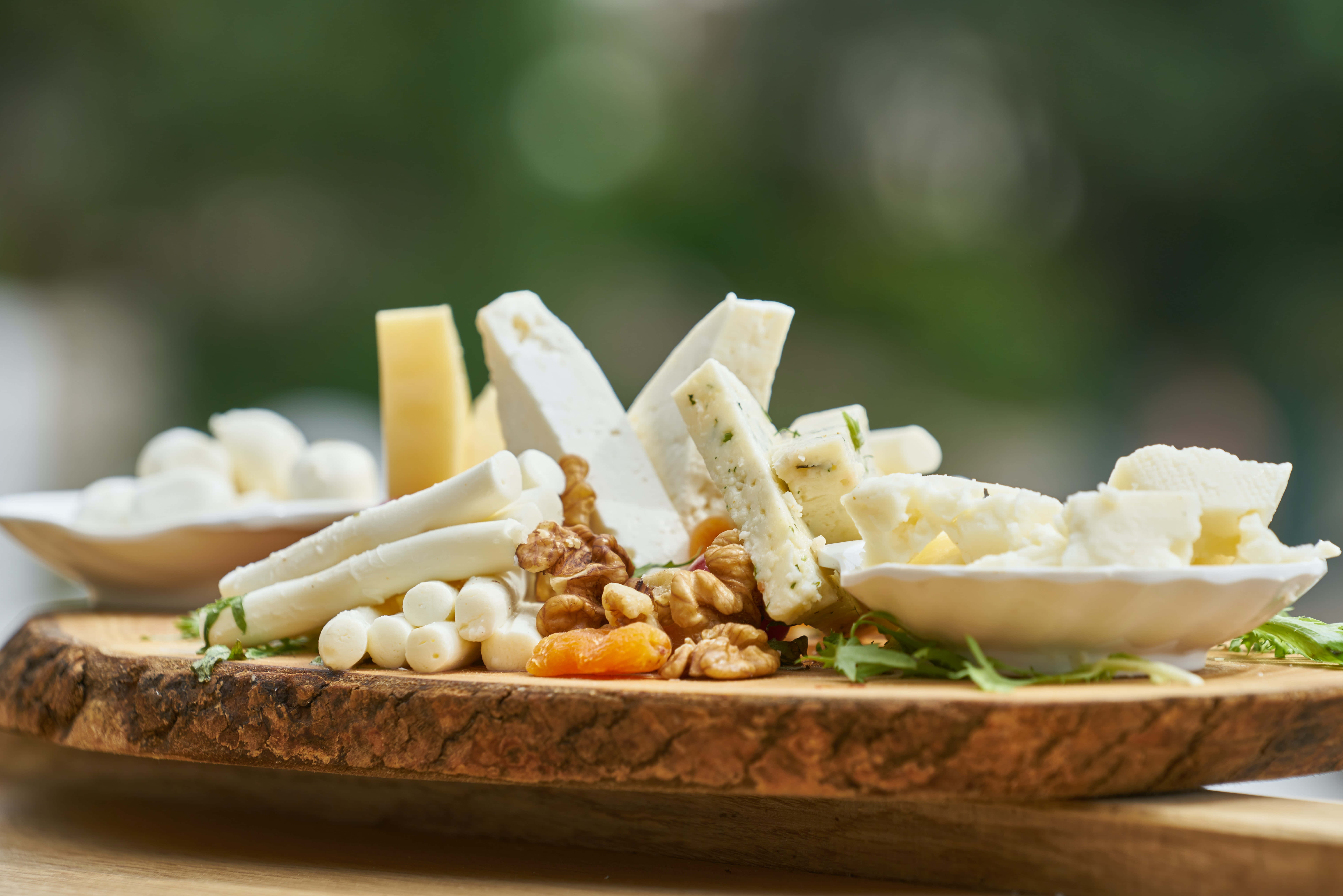 Cheese 桌布 壁紙 — 一塊質樸的木板上，藝術地擺放著各式芝士、堅果和乾果，背景是柔和的綠色模糊效果。