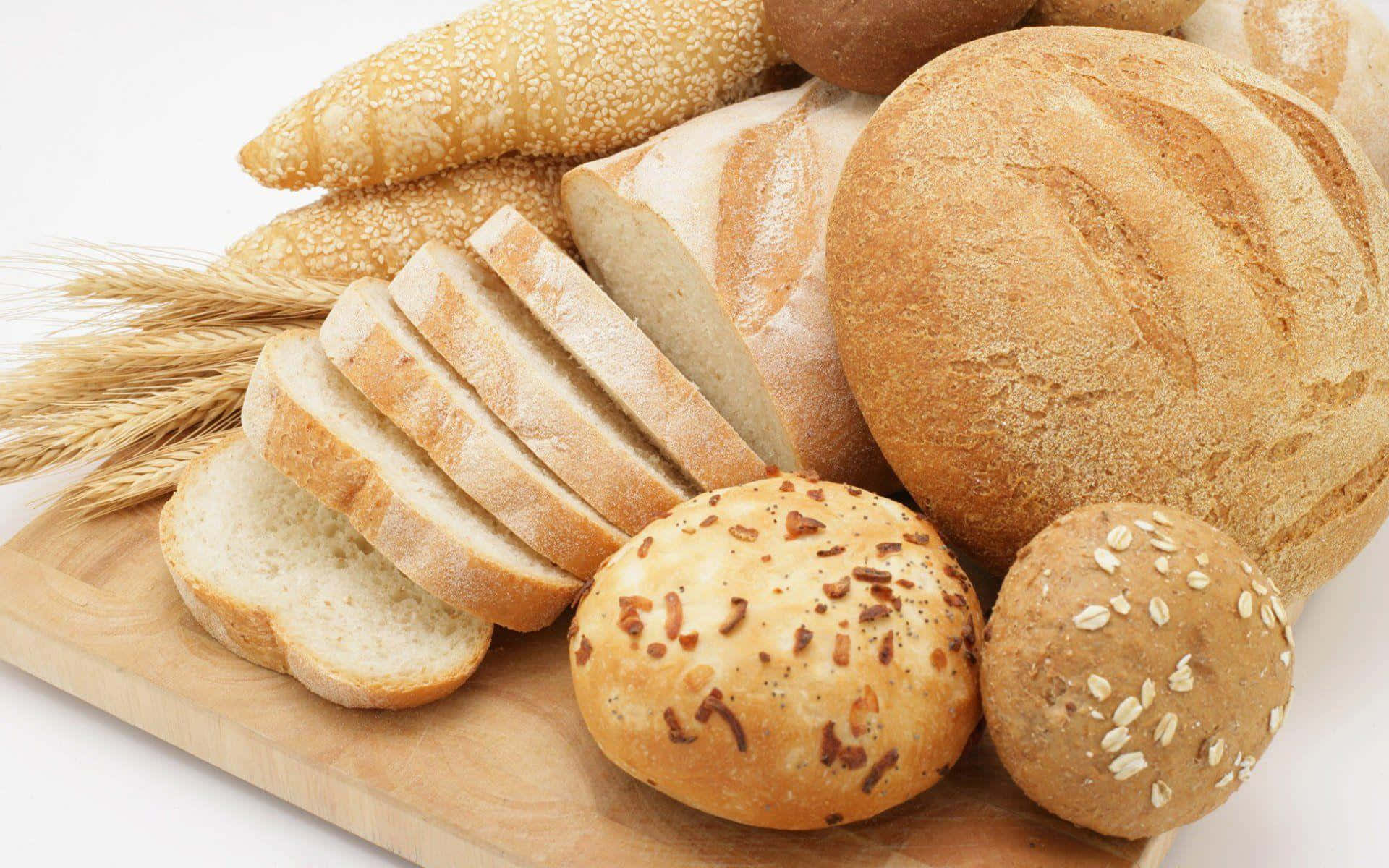 Bakery 桌布 壁紙 — 一塊質樸的木板上展示著各種新鮮麵包，包括切片白麵包卷和種子麵包，旁邊放著小麥穗。