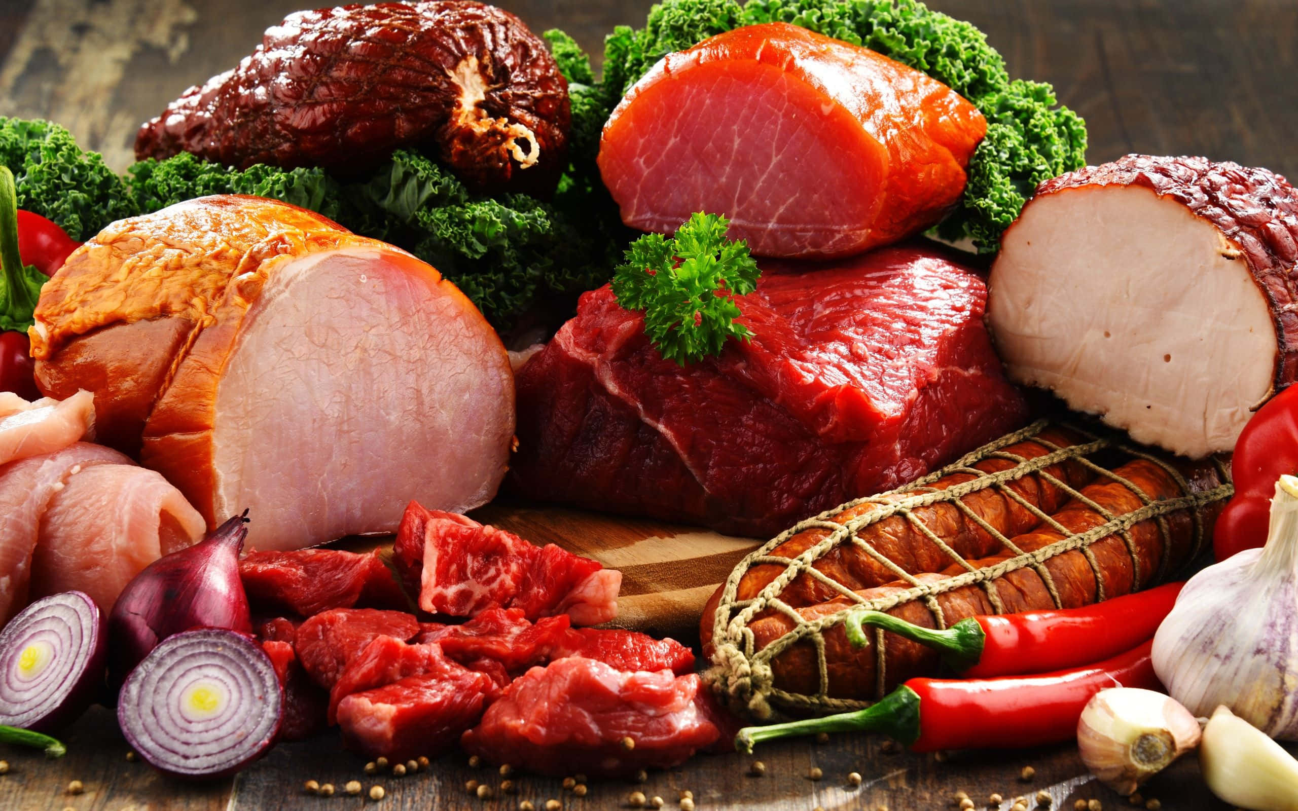 Red Meat 桌布 壁紙 — 一塊質樸的木板上展示著各種生肉和醃製肉類，並以新鮮香草和鮮紅色的辣椒點綴。