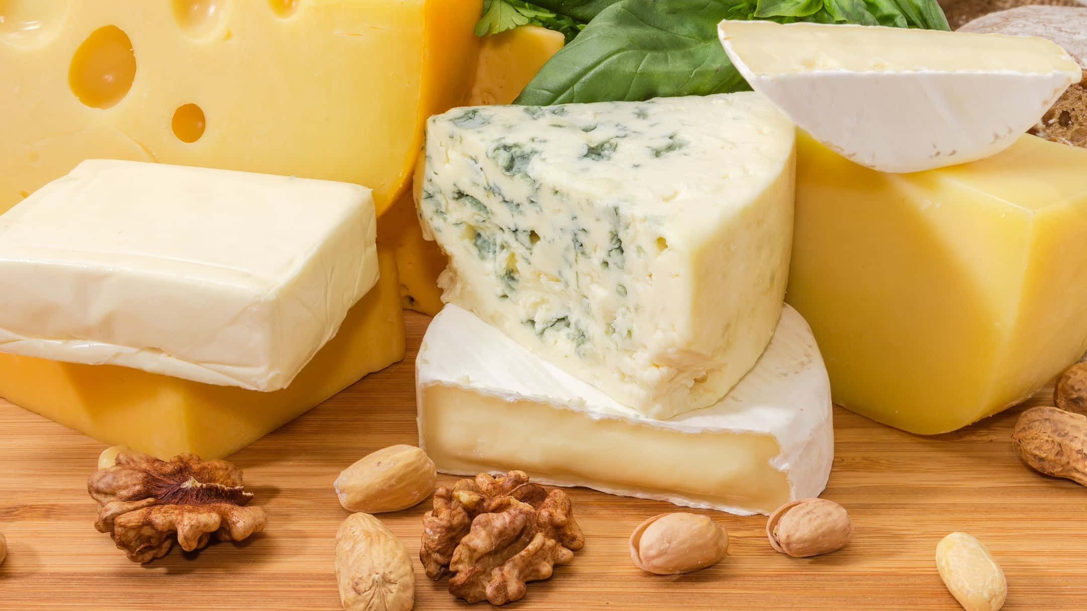 Cheese 桌布 壁紙 — 一塊質樸的木板上展示著各種芝士，包括藍紋芝士、布里芝士和車打芝士，以及核桃和杏仁。