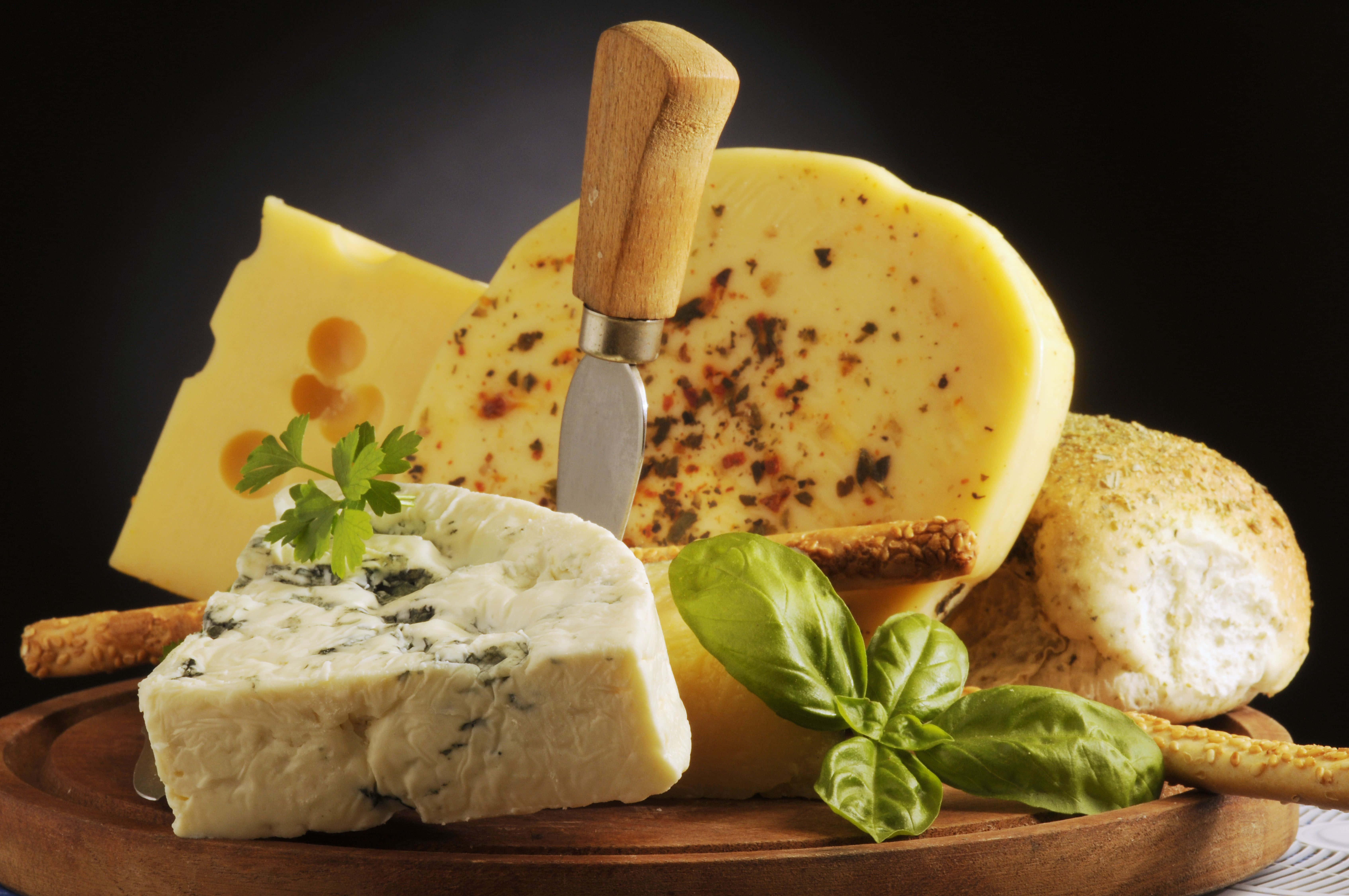 Cheese 桌布 壁紙 — 一塊質樸的木板上展示著各種芝士，配以新鮮羅勒和麵包棒，背景為深色。