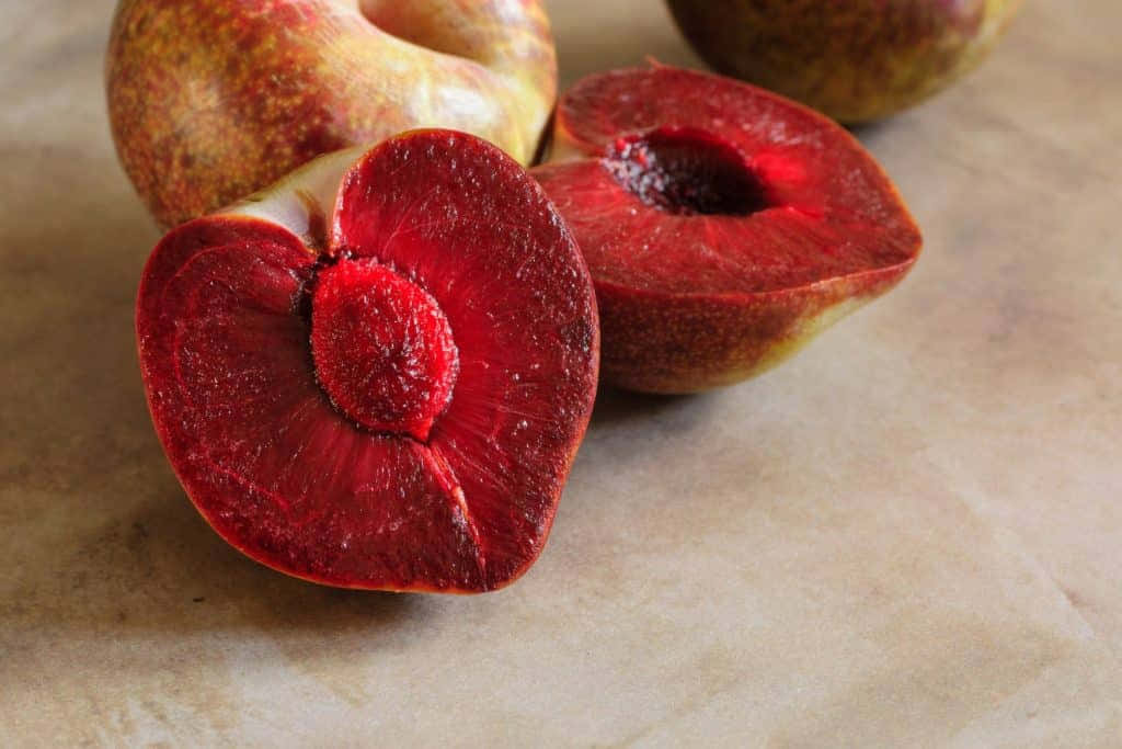 Red Plum 桌布 壁紙 — 一塊鮮紅色的切片桃子，在紋理石面上與整個桃子一起展現其多汁的內部。