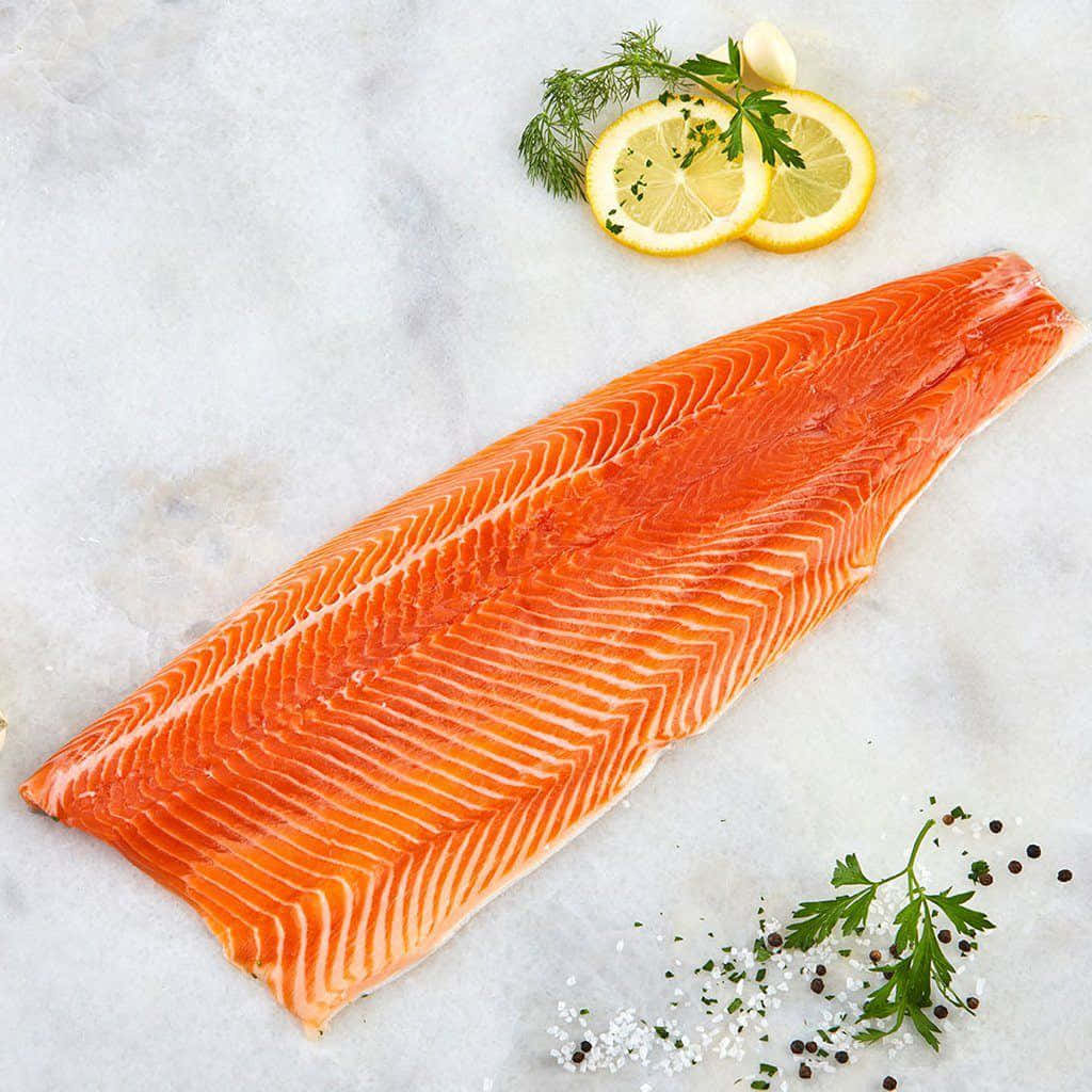Salmon 桌布 壁紙 — 一塊鮮豔的橙色三文魚柳放在白色大理石表面上，旁邊有檸檬片、新鮮香草和鹽胡椒。