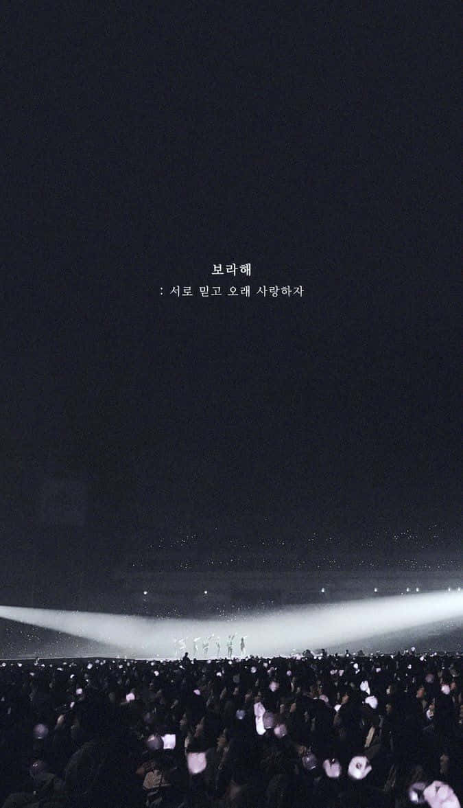 Aesthetic Korean 桌布 壁紙 — 一大群人在夜晚手持發光手機，在明亮的舞台燈光下，上方漂浮著韓文文字。