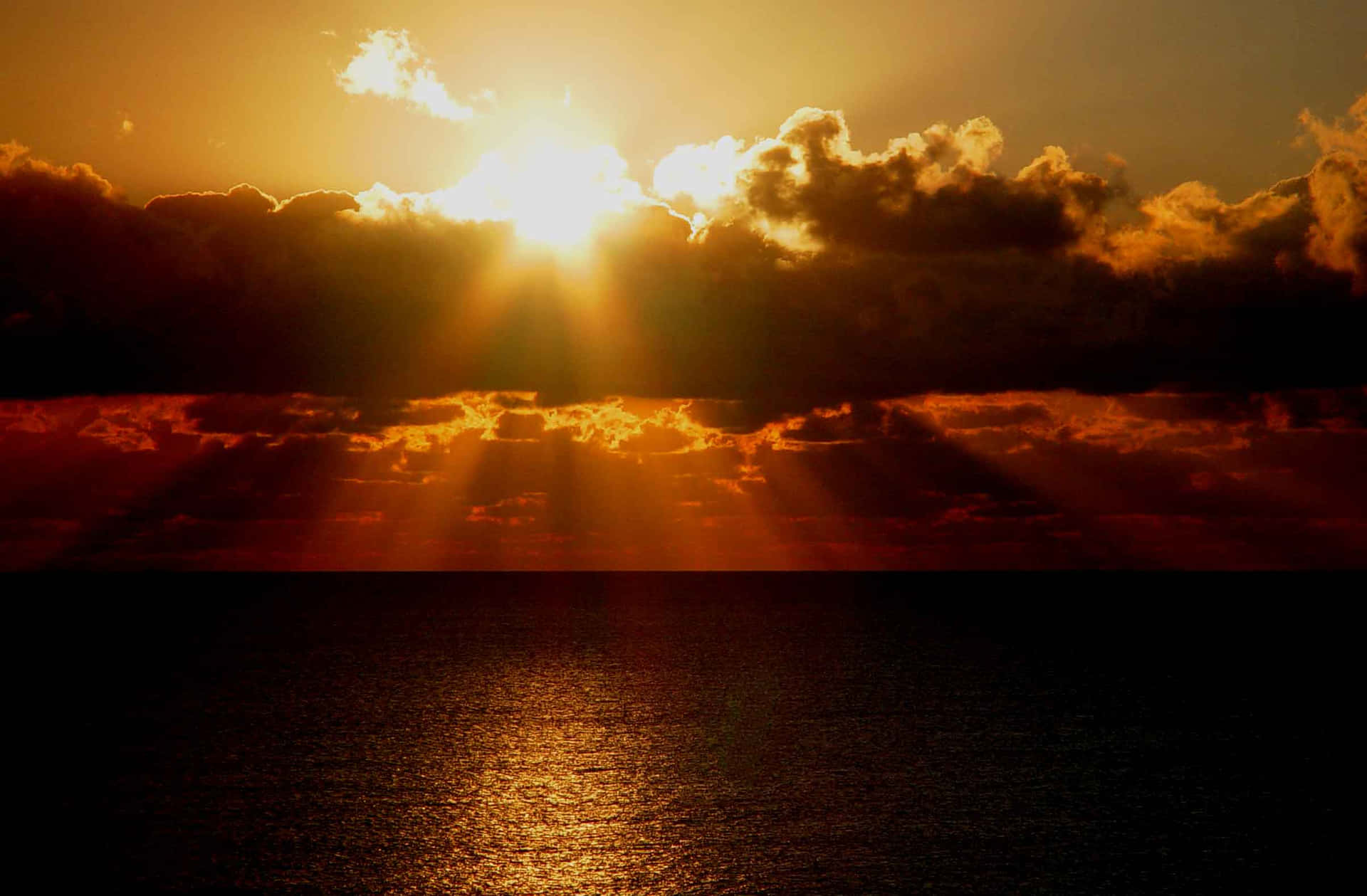 夕陽穿過雲層，照射在黃昏時分平靜的海面上。