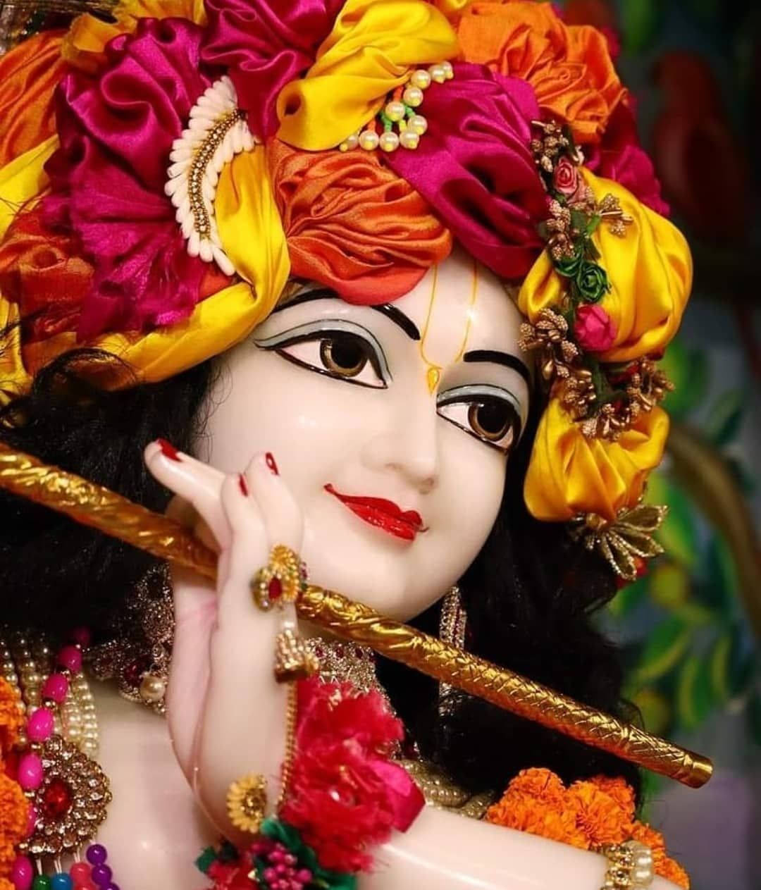 Krishna HD 桌布 壁紙 — 一尊充滿活力的克里希納神像，裝飾著色彩繽紛的絲綢花朵、黃金首飾和紅唇，將笛子放在唇邊。