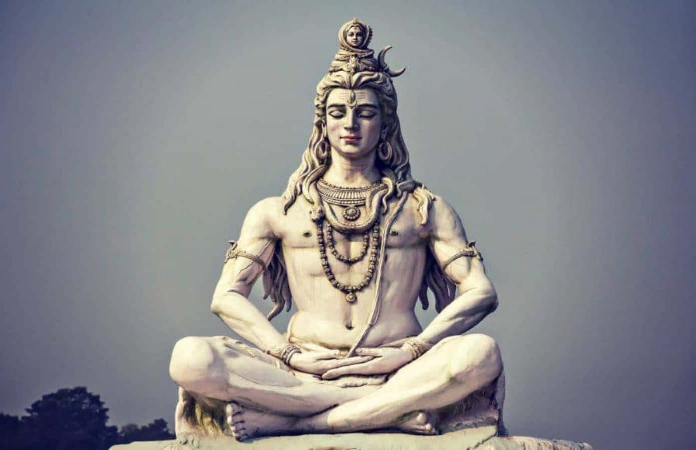 Lord Shiva 桌布 壁紙 — 一尊寧靜的白色濕婆石像，呈冥想姿勢，頭戴新月冠冕，頸掛蛇形項鍊，背景是柔和天空。