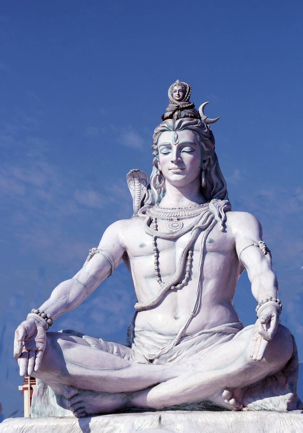 bholenath 桌布 壁紙 — 一尊寧靜的白色石雕濕婆神以蓮花坐姿在清澈藍天下冥想。