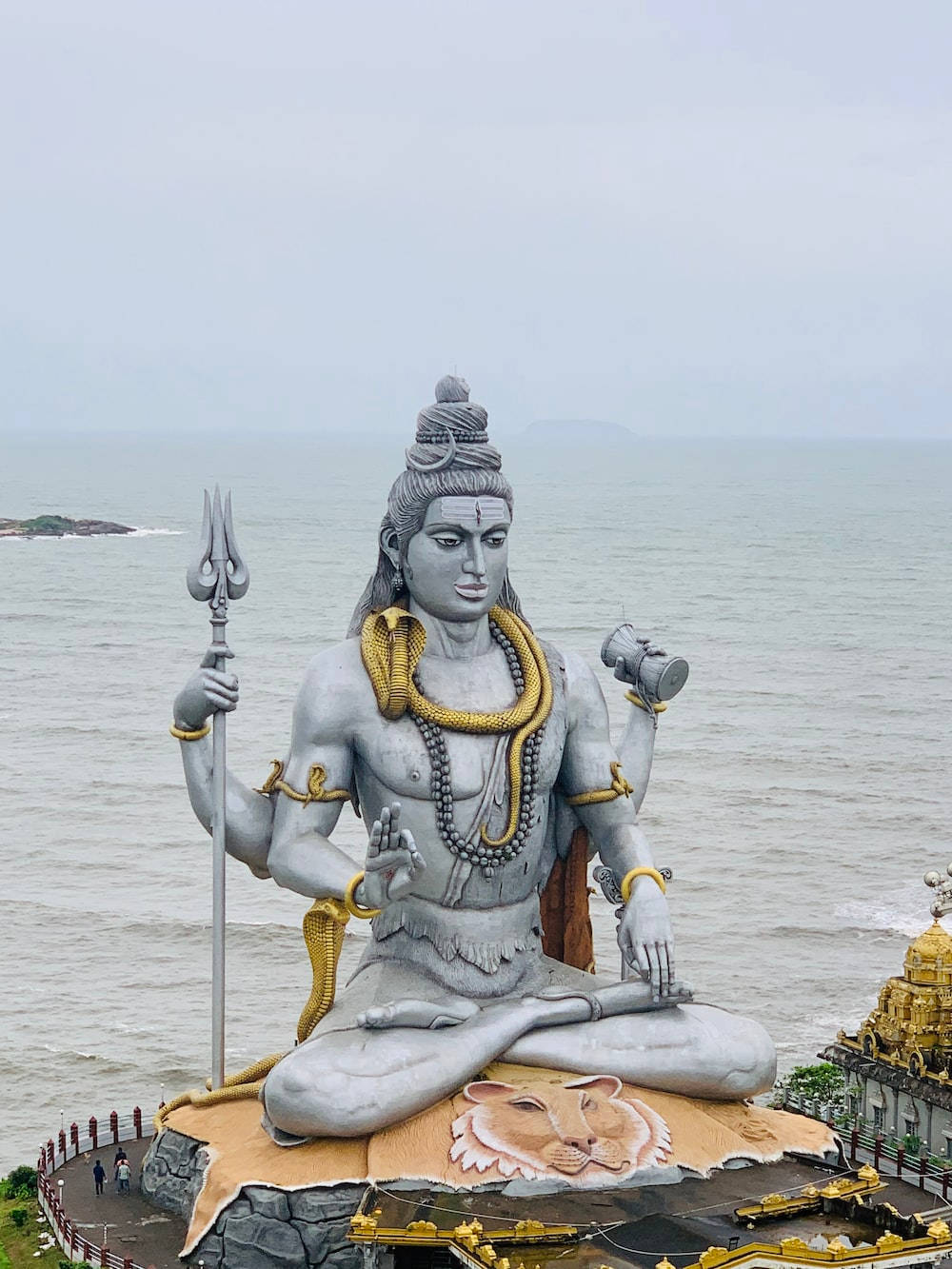 India 桌布 壁紙 — 一尊巨大的灰色濕婆神石像在獅子上冥想，俯瞰陰天下的海洋。