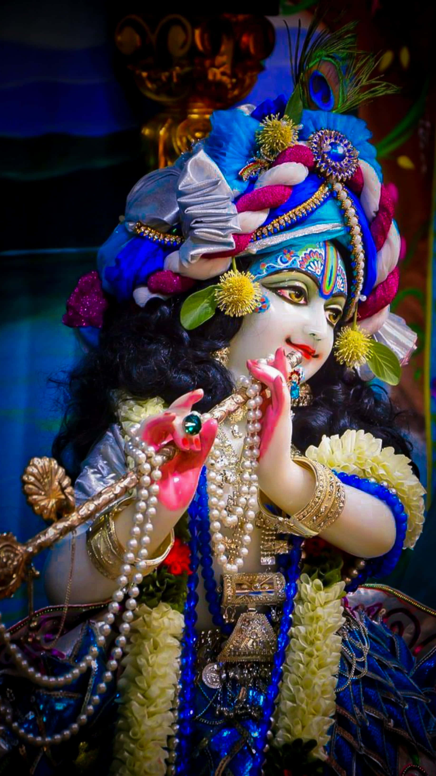 Radha Krishna 桌布 壁紙 — 一尊色彩繽紛的神像，戴著藍色和粉紅色的頭飾、孔雀羽毛和珍珠首飾，正在吹奏長笛。