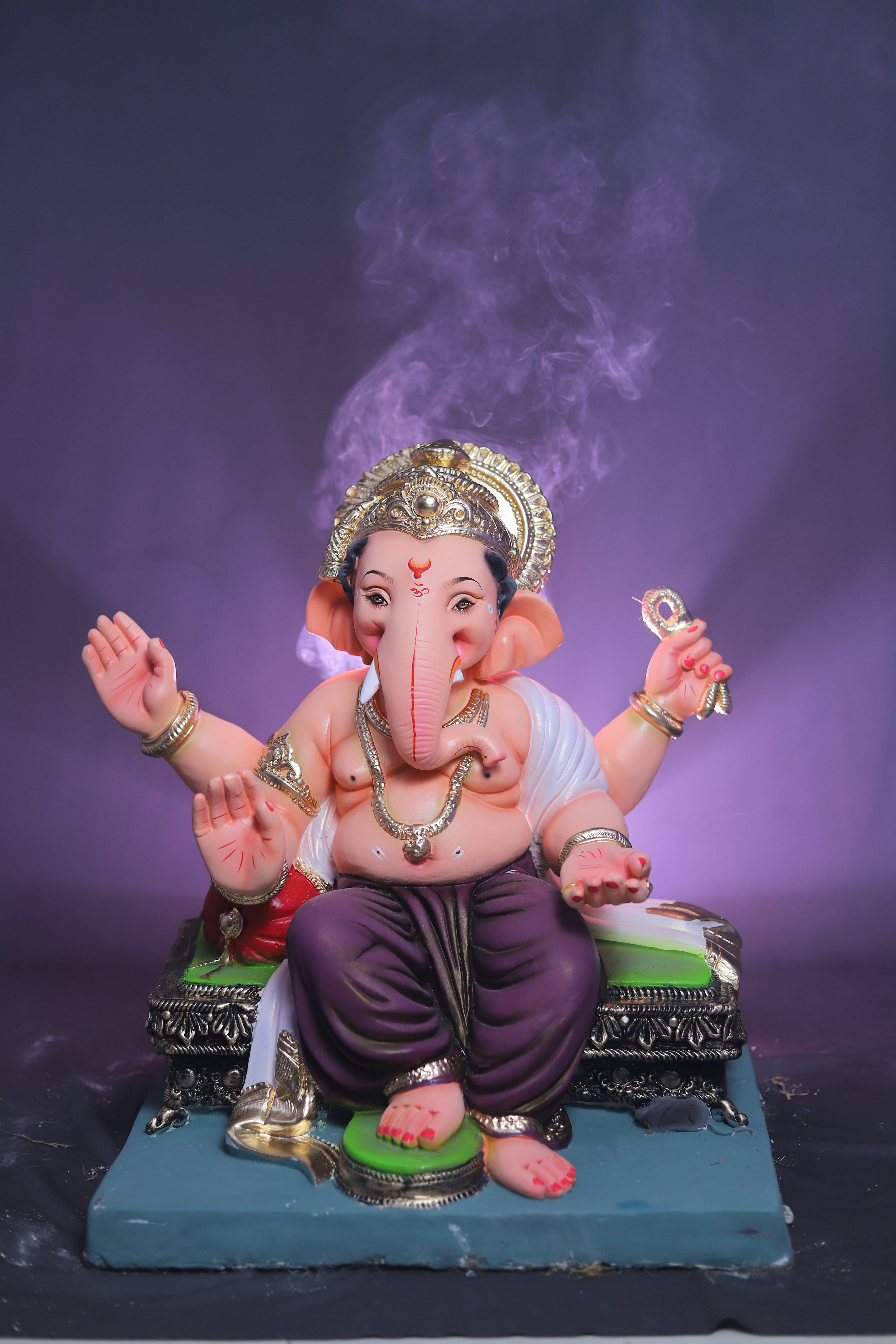 ganesh iPhone 桌布 壁紙 — 一尊色彩繽紛的象神像，身後有紫色煙霧升起，背景為深紫色。