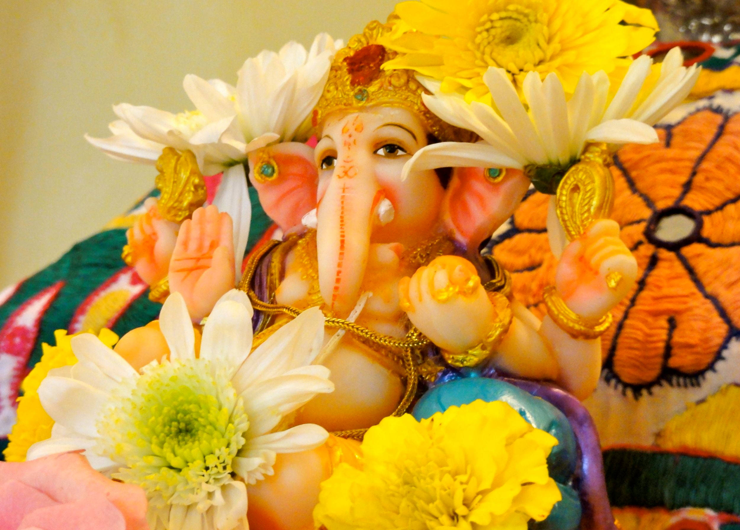 Ganesh Chaturthi 桌布 壁紙 — 一尊色彩繽紛的象神像，飾以黃色和白色花朵，置於鮮豔的刺繡布料上。