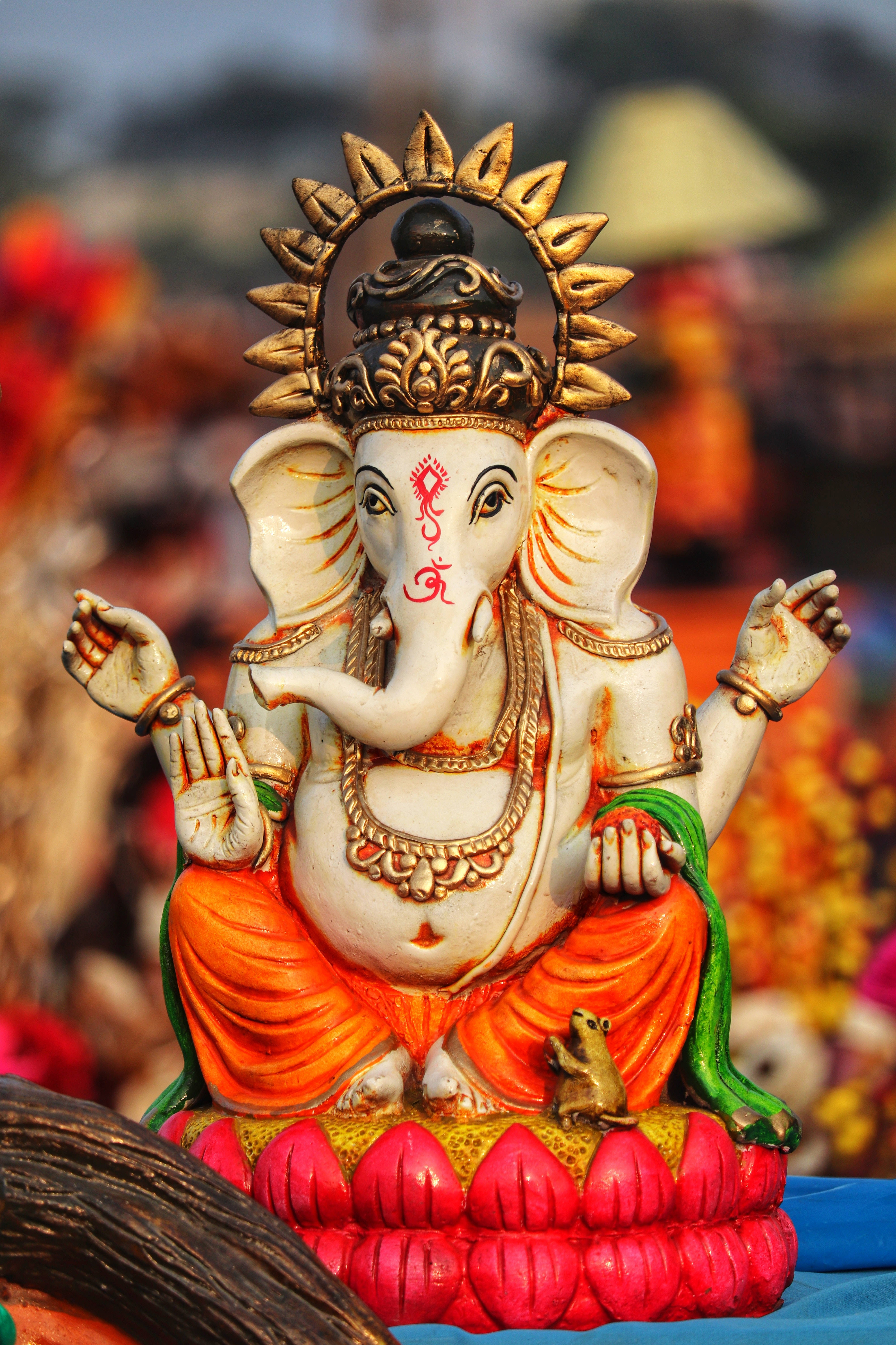 ganesh iPhone 桌布 壁紙 — 一尊色彩鮮豔的象神像，頭戴金色皇冠，身穿橙色腰布，安詳地坐在紅色蓮花座上。